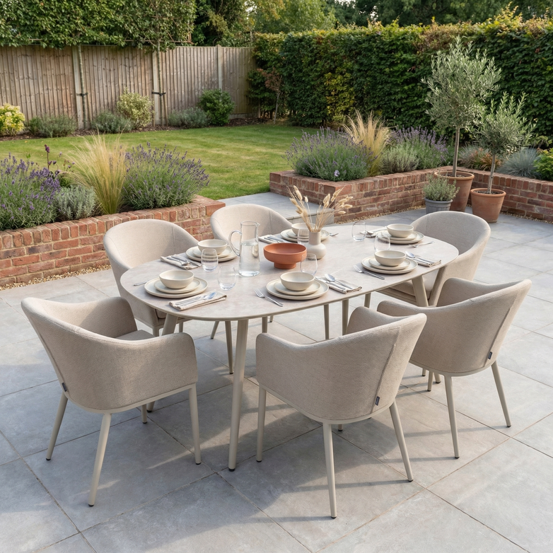 Enjoy outdoor dining with the Luna 6 Seat Outdoor Fabric Oval Ceramic Dining Set in Fawn, featuring beige all-weather fabric chairs and a stylish oval table—perfect for your patio with a garden view.