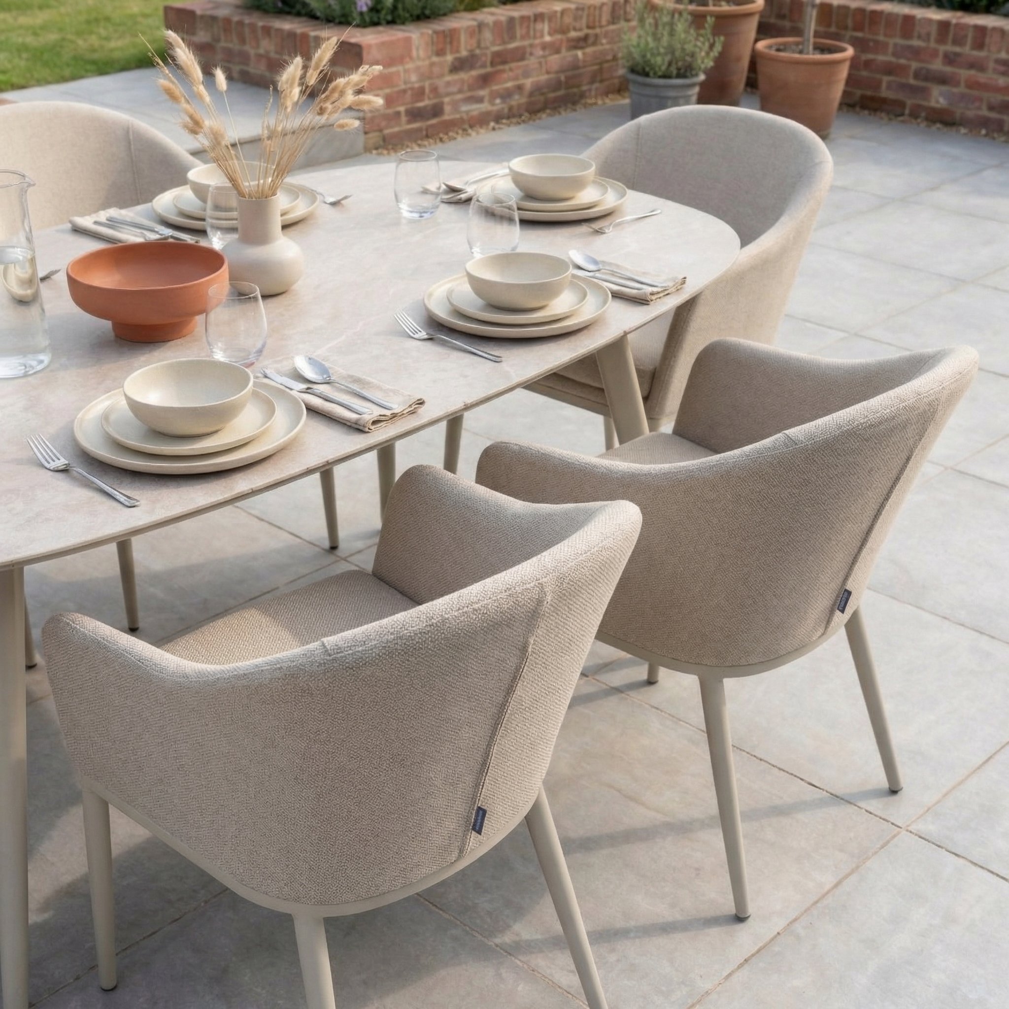 Luna 6 Seat Outdoor Fabric Oval Ceramic Dining Set in Fawn, shown with plates, glasses, and a dried grass vase on a tiled patio—ideal for stylish all-weather gatherings.