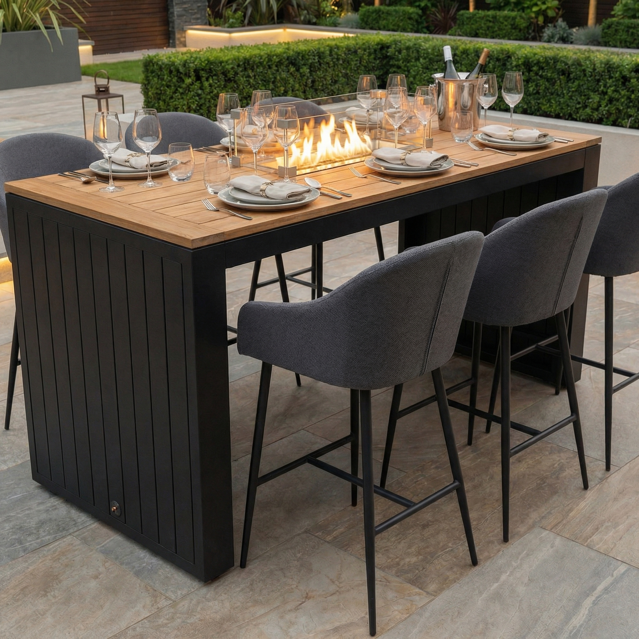 The Luna 6 Seat Outdoor Fabric Teak Firepit Bar Set in Grey includes gray chairs, a teak firepit table, plus dishes and glassware for outdoor dining in any weather.