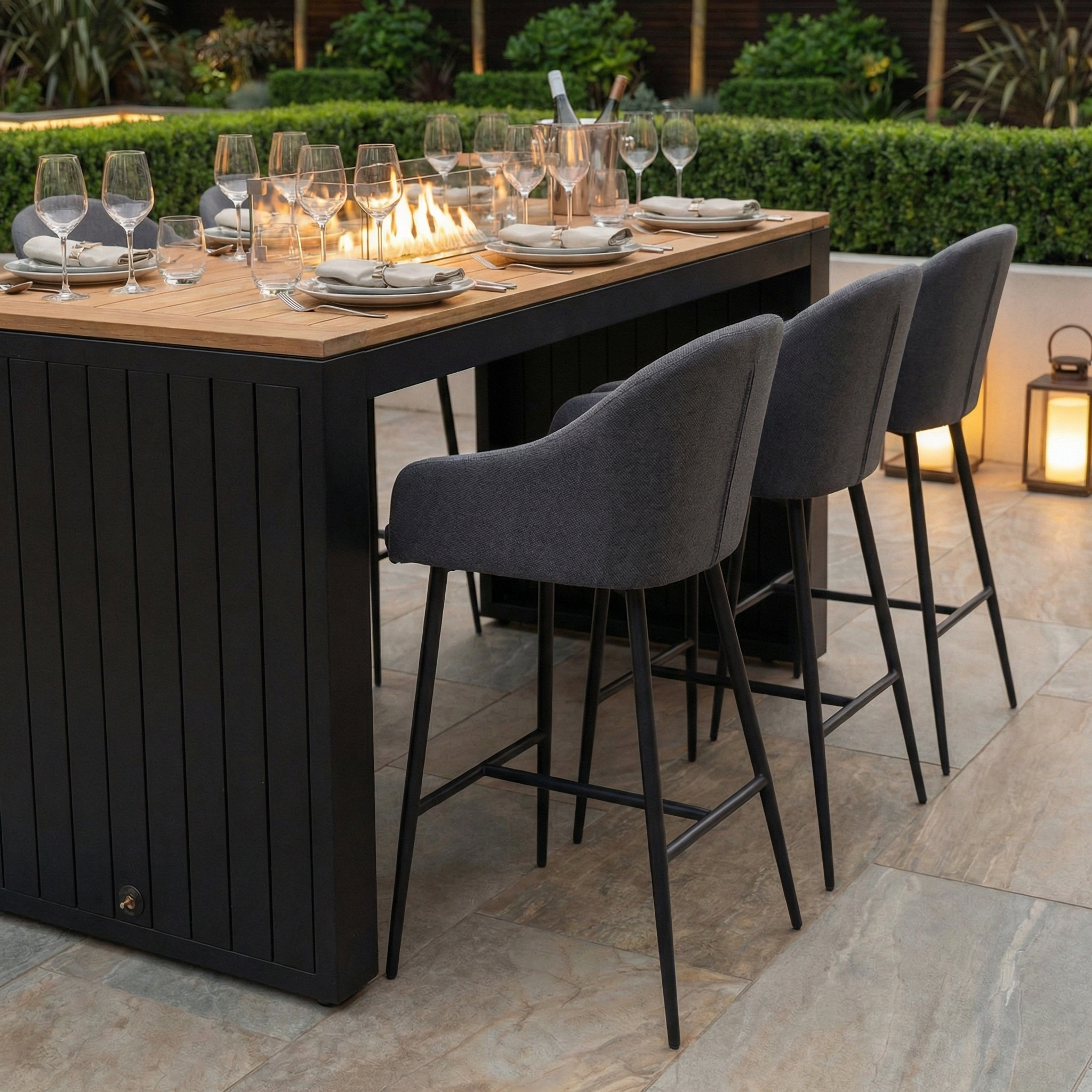 The Luna 6 Seat Outdoor Fabric Teak Firepit Bar Set in Grey is set for dinner, featuring a modern all-weather dining table with gray chairs and wine glasses.