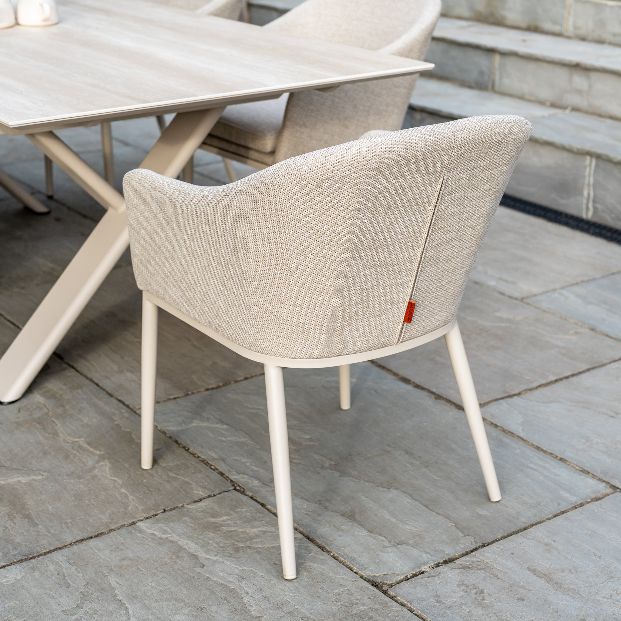 The Luna 6 Seat Outdoor Fabric Dining Set with Albatross Extending Table in Fawn features light beige chairs with all-weather fabric and white legs, perfect for creating an inviting outdoor dining space on your patio.