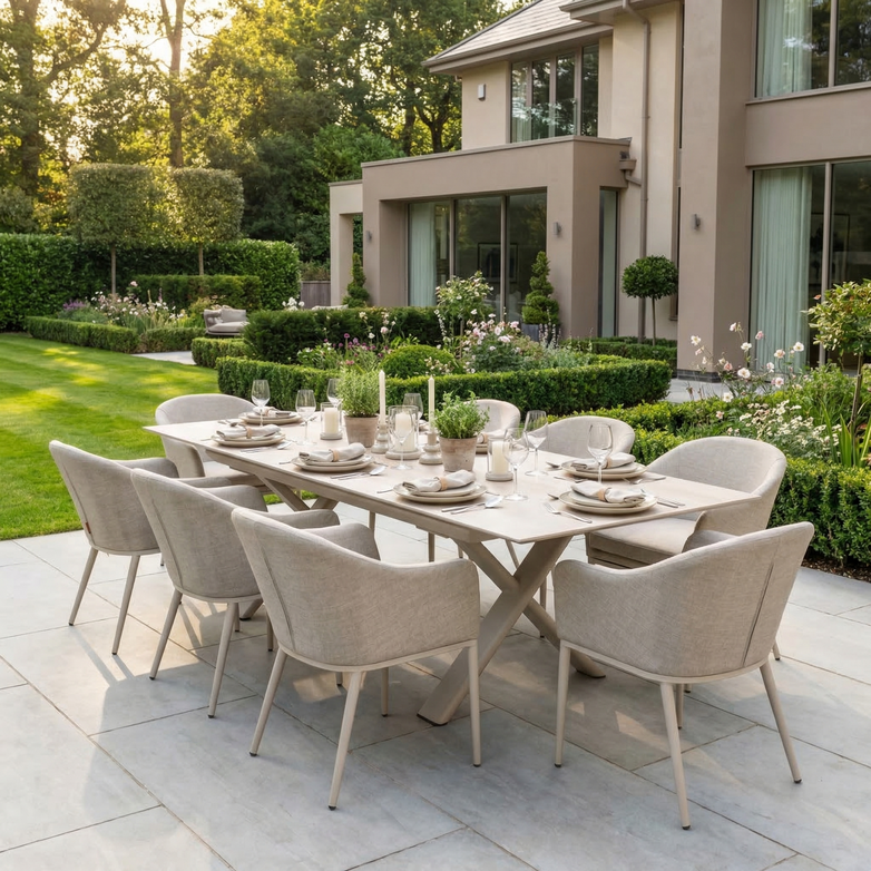 The Luna 8 Seat Outdoor Fabric Dining Set with Albatross Extending Table in Fawn is arranged for dining in a landscaped garden beside a modern house, offering versatile seating for gatherings.
