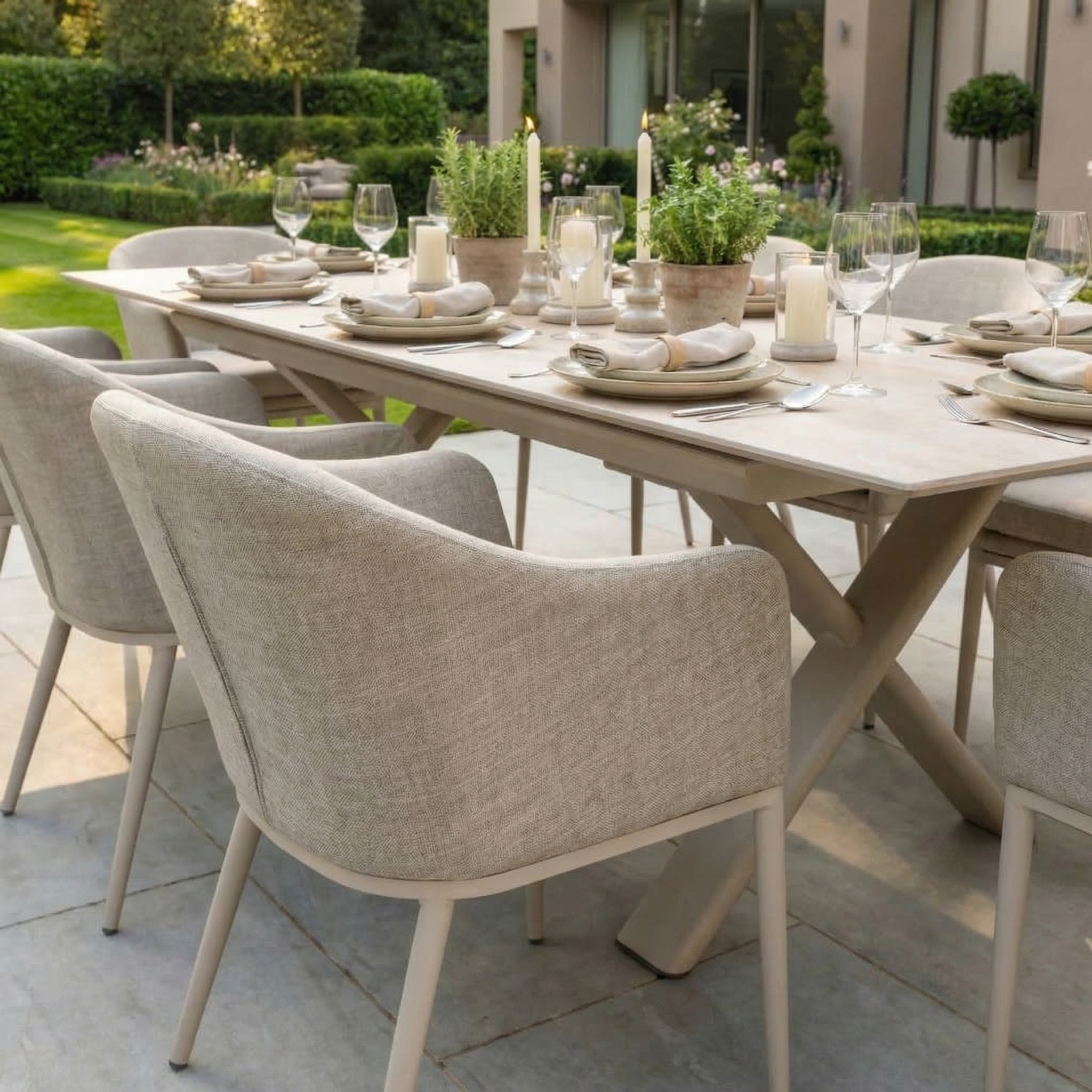 The Luna 8 Seat Outdoor Fabric Dining Set with Albatross Extending Table in Fawn, paired with candles and potted plants, creates a charming patio dining scene in the garden.