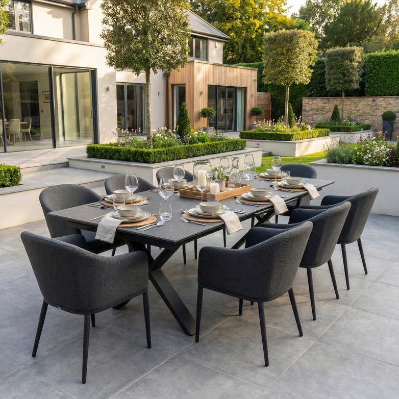 The Luna 8 Seat Outdoor Fabric Dining Set with Albatross Extending Table in Grey is arranged for dining on a patio in a landscaped garden.