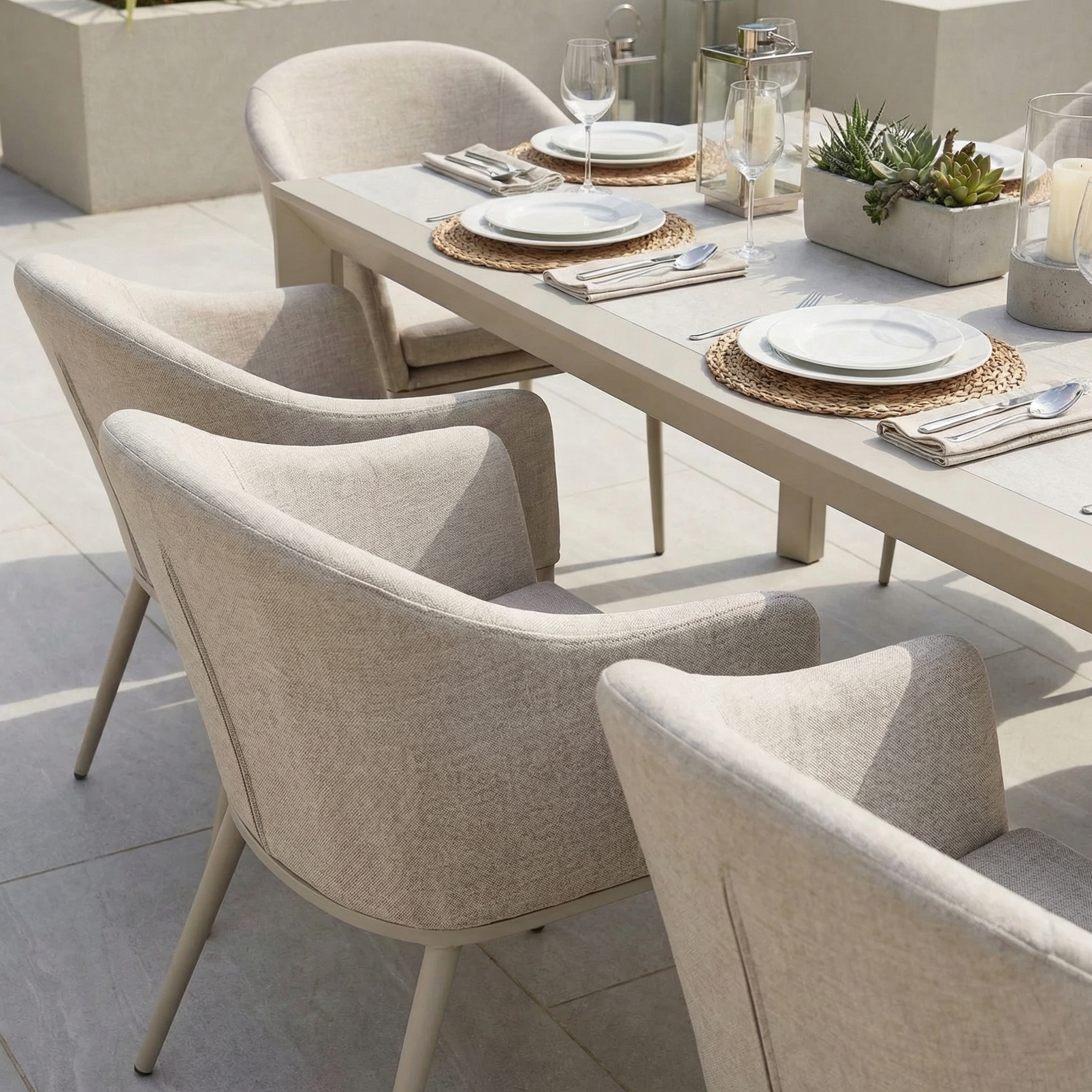The Luna 8 Seat Outdoor Fabric Extending Ceramic Dining Set in Fawn, styled with plates, glasses, and candles on a sunny patio, features stain-proof chairs—perfect for any outdoor gathering.