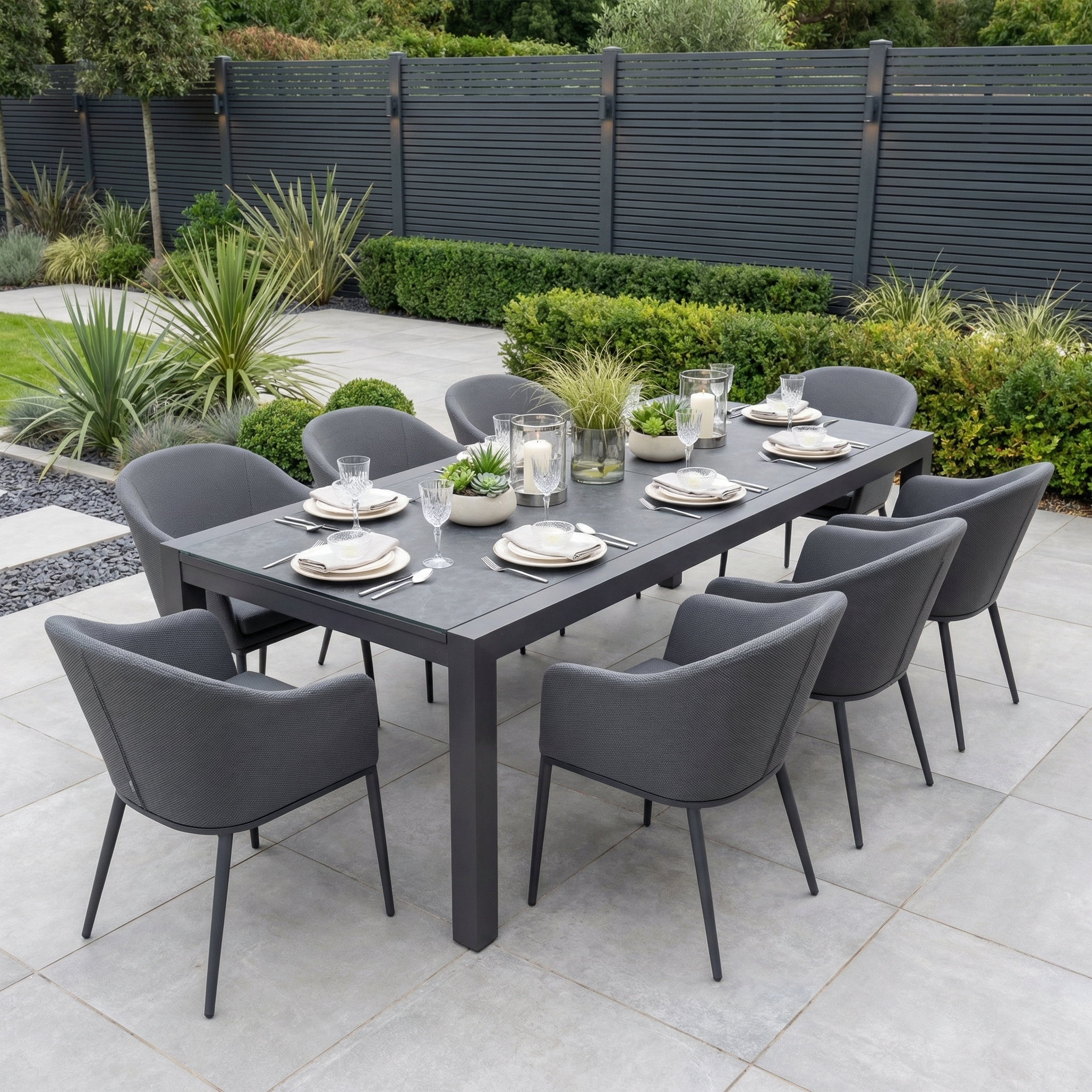 Host stylish gatherings with the Luna 8 Seat Outdoor Fabric Extending Ceramic Dining Set in Grey—featuring eight gray chairs and a set table, this stain-proof garden furniture is ideal for modern outdoor dining on a tiled patio with potted plants.