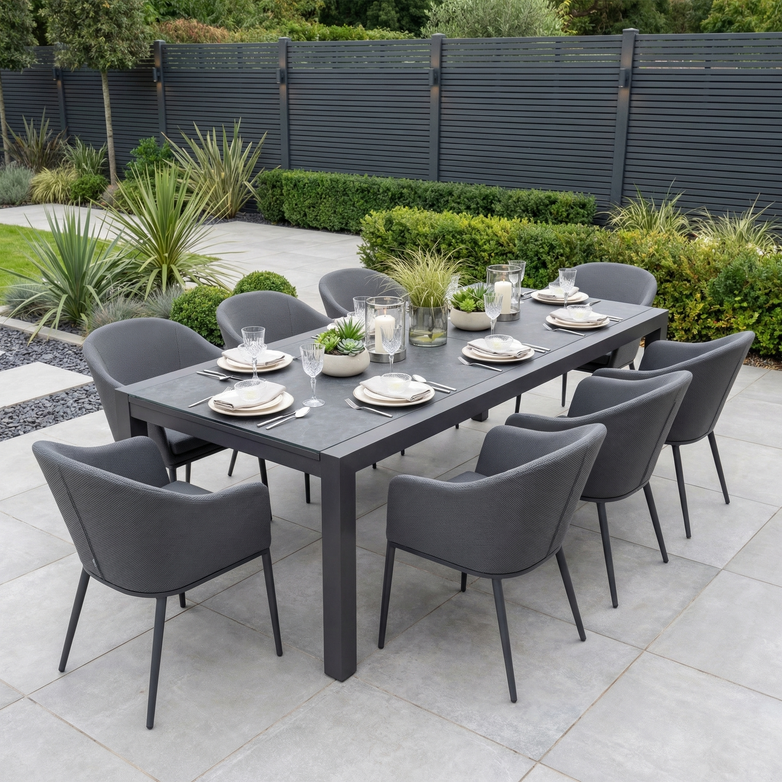Host stylish gatherings with the Luna 8 Seat Outdoor Fabric Extending Ceramic Dining Set in Grey—featuring eight gray chairs and a set table, this stain-proof garden furniture is ideal for modern outdoor dining on a tiled patio with potted plants.
