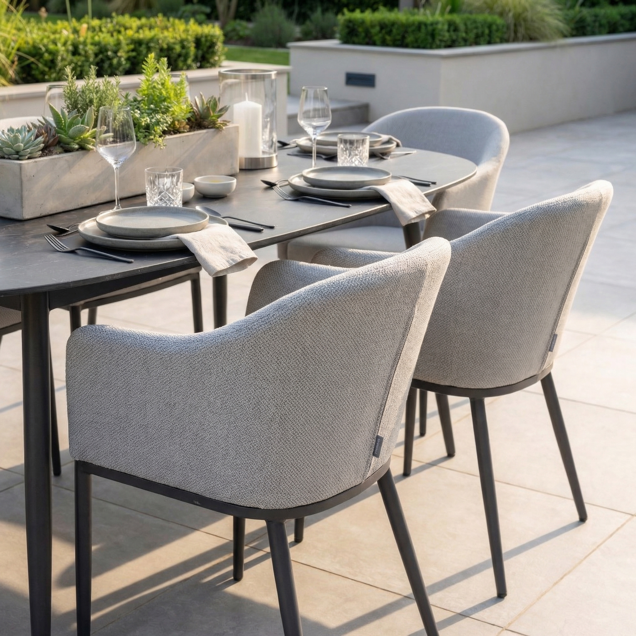The Luna 8 Seat Outdoor Fabric Oval Ceramic Dining Set in Oyster Grey includes gray cushioned chairs, tableware, and succulent centerpieces—crafted from all-weather materials for lasting outdoor style.