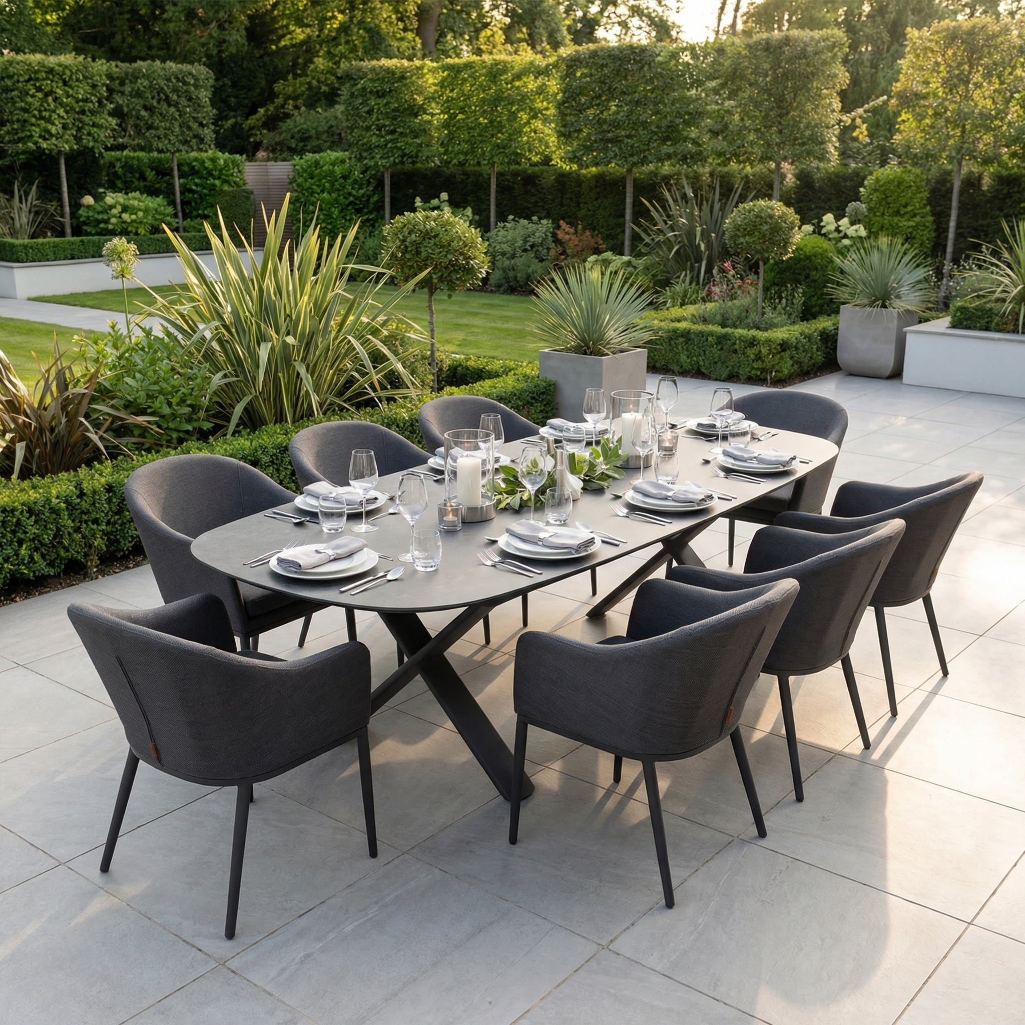 The Luna 8 Seat Outdoor Fabric Oval Dining Set with Albatross Extending Table in Grey features UV resistant materials and seats eight, ideal for stylish outdoor dining on a tiled patio surrounded by lush greenery.