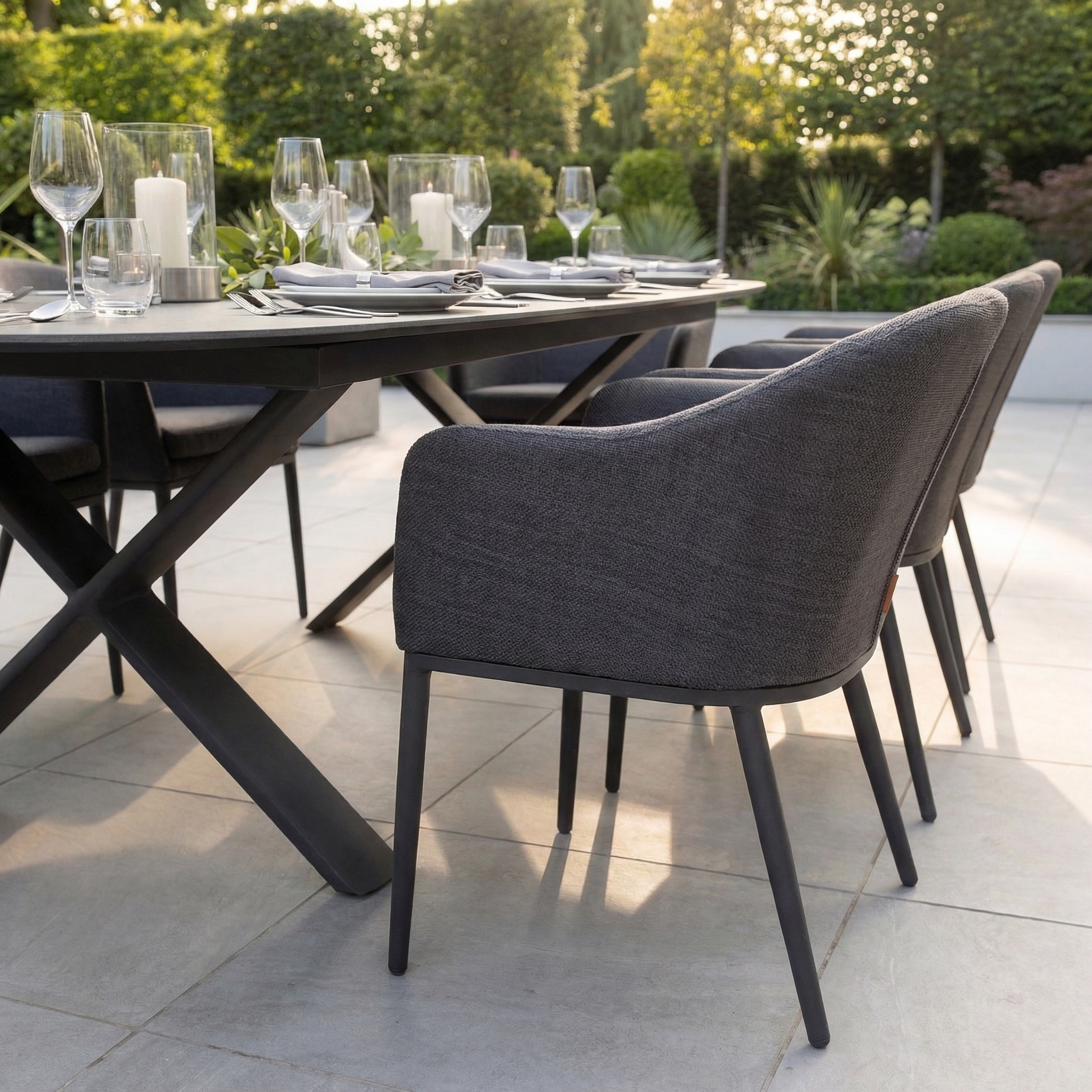 The Luna 8 Seat Outdoor Fabric Oval Dining Set with Albatross Extending Table in Grey features cushioned chairs, glassware, and candles arranged on a stylish patio.