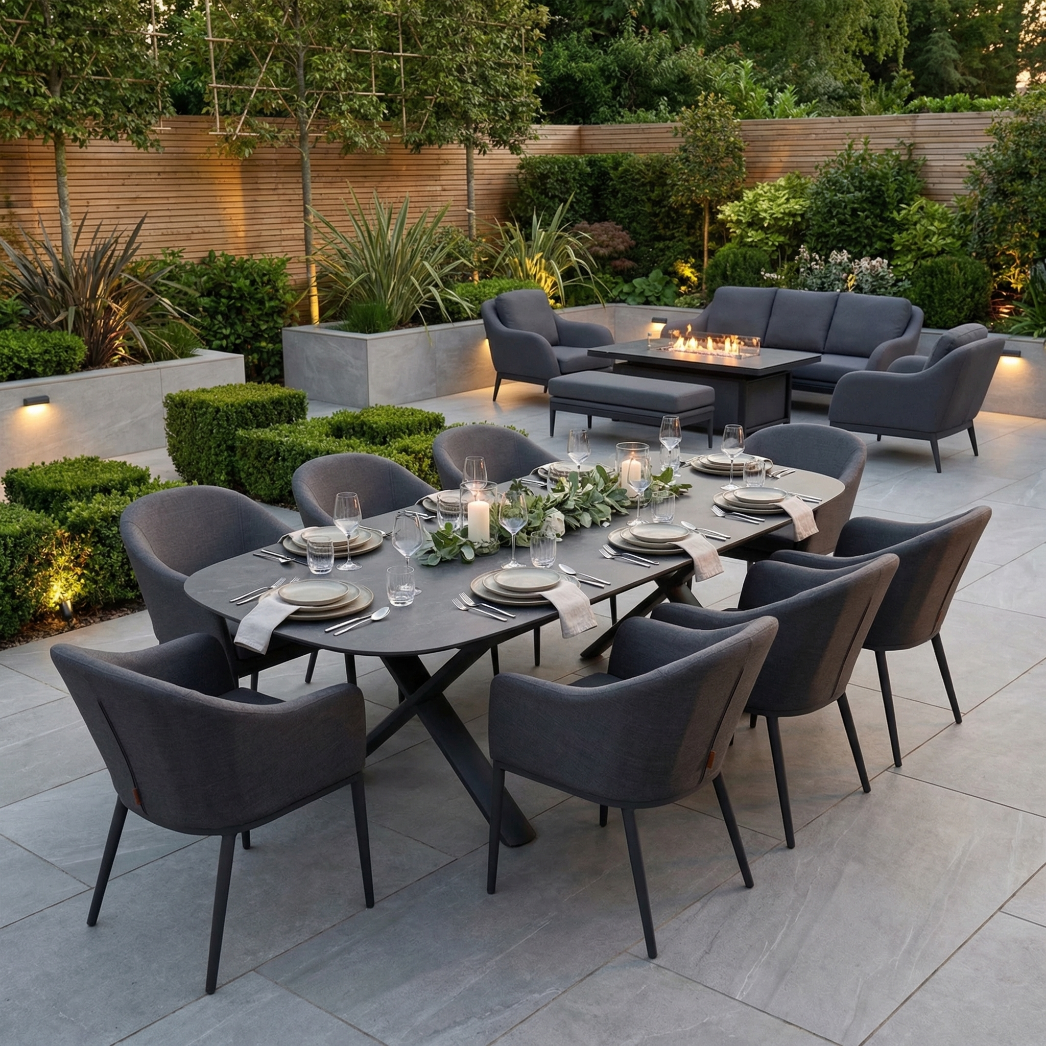 Modern patio with greenery and a fire pit, featuring the Luna 8 Seat Outdoor Fabric Oval Dining Set with Albatross Extending Table in Grey, plus comfortable lounge chairs.