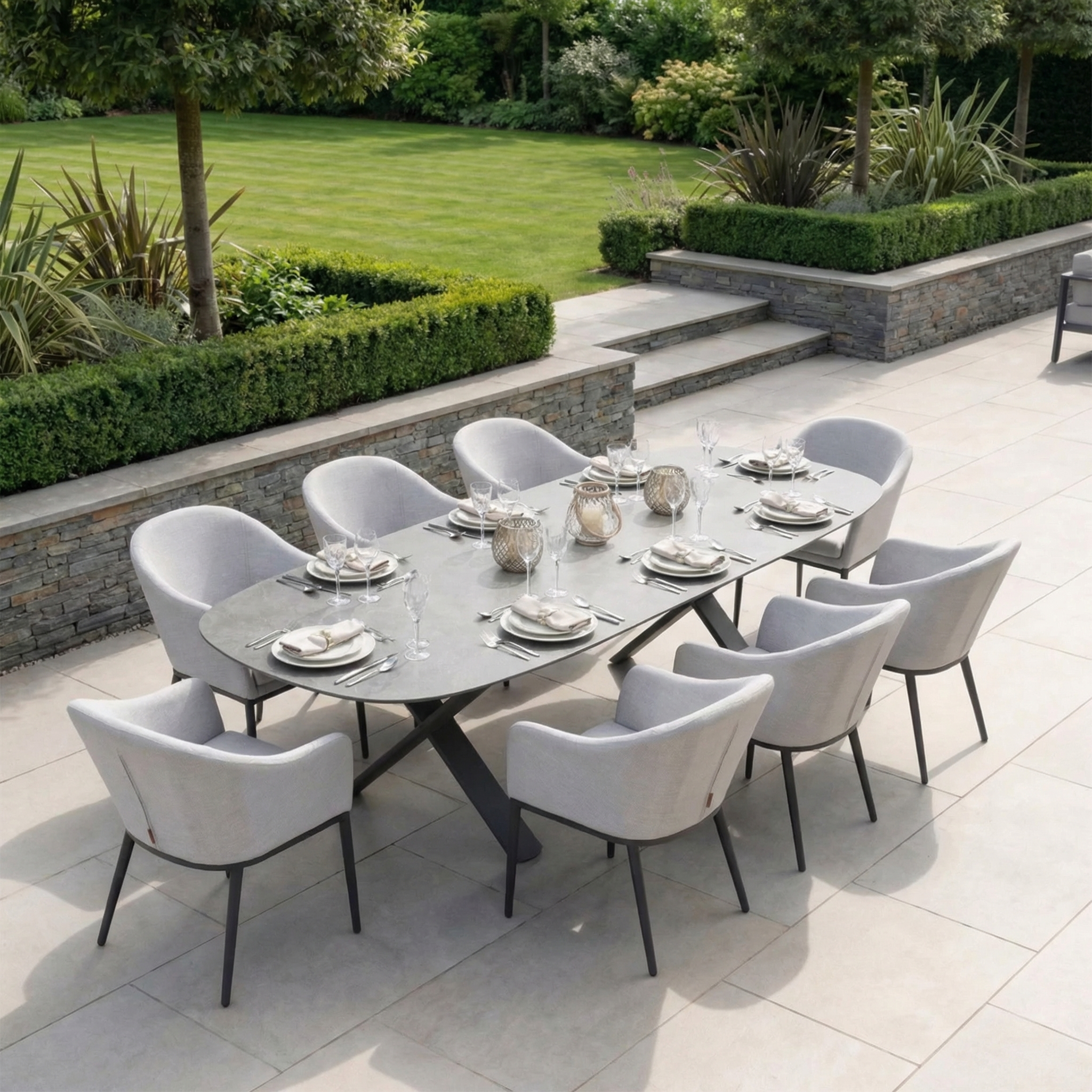 The Luna 8 Seat Outdoor Fabric Oval Dining Set with Albatross Extending Table in Oyster Grey, featuring UV resistant cushions, is nestled amid manicured gardens.