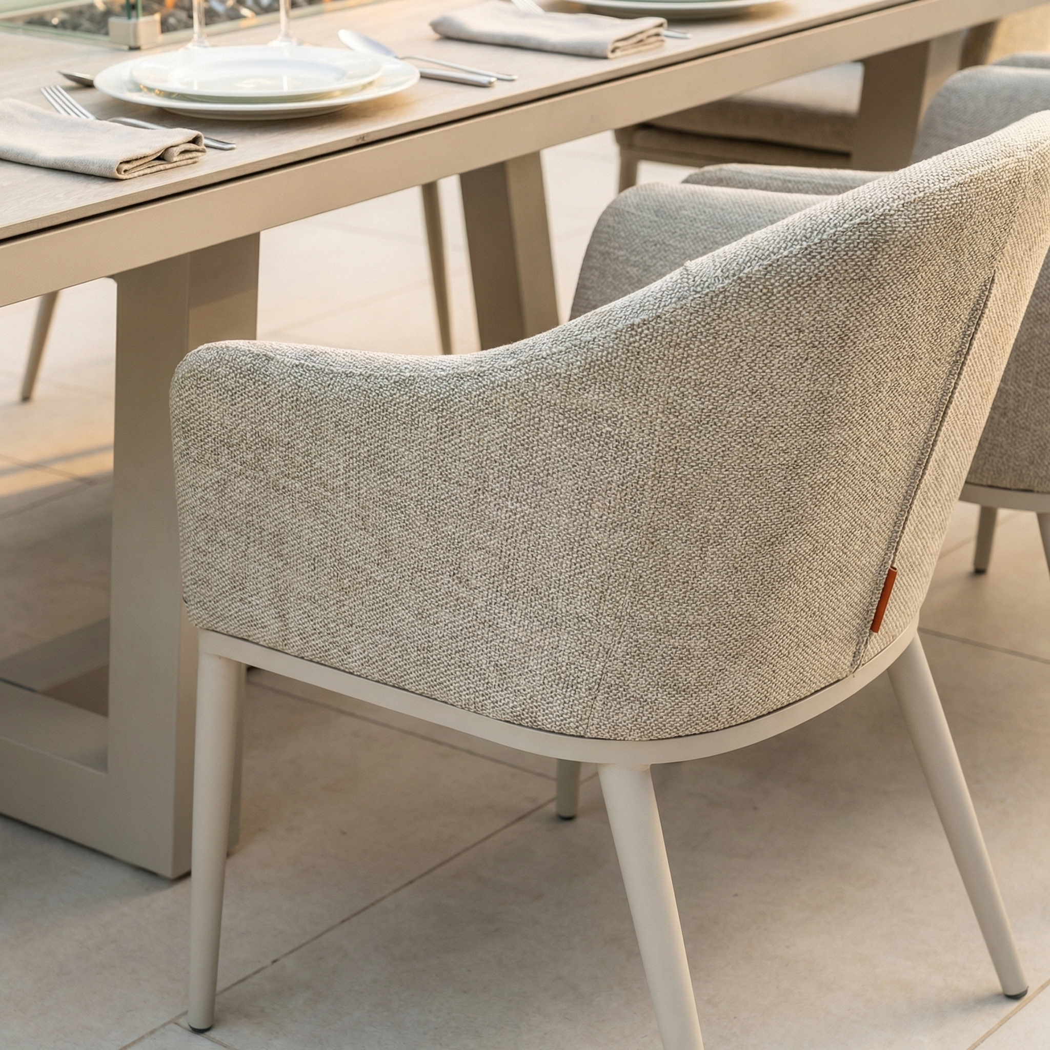 The Luna 8 Seat Outdoor Fabric Rectangular Ceramic Firepit Dining Set in Fawn, with light gray chairs and an elegant table setting, is perfect for stylish patio dining around your firepit.