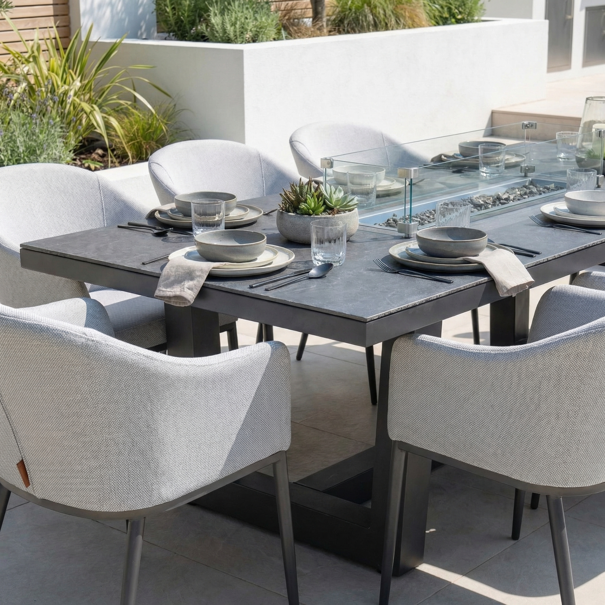 The Luna 8 Seat Outdoor Fabric Rectangular Ceramic Firepit Dining Set in Oyster Grey features modern all-weather chairs, a stylish ceramic table, place settings, glasses, and a succulent centerpiece.