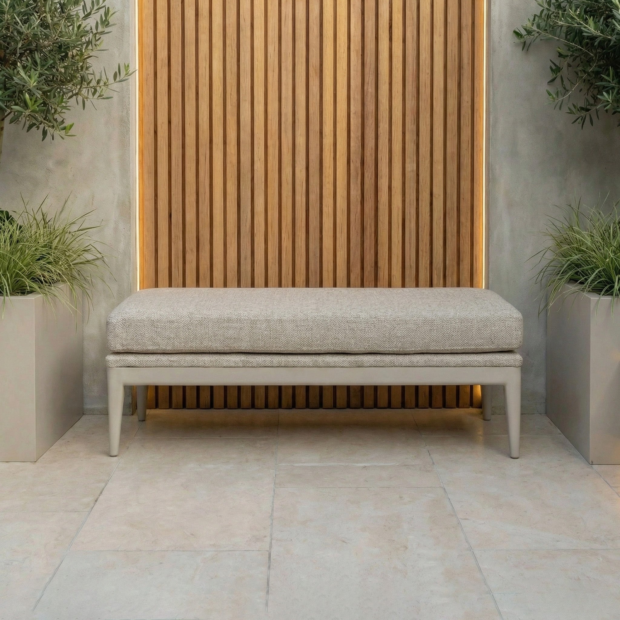 Luna Bench in Fawn set against a wooden slat wall, with green plants in square gray planters on a tile floor—ideal all-weather outdoor seating.