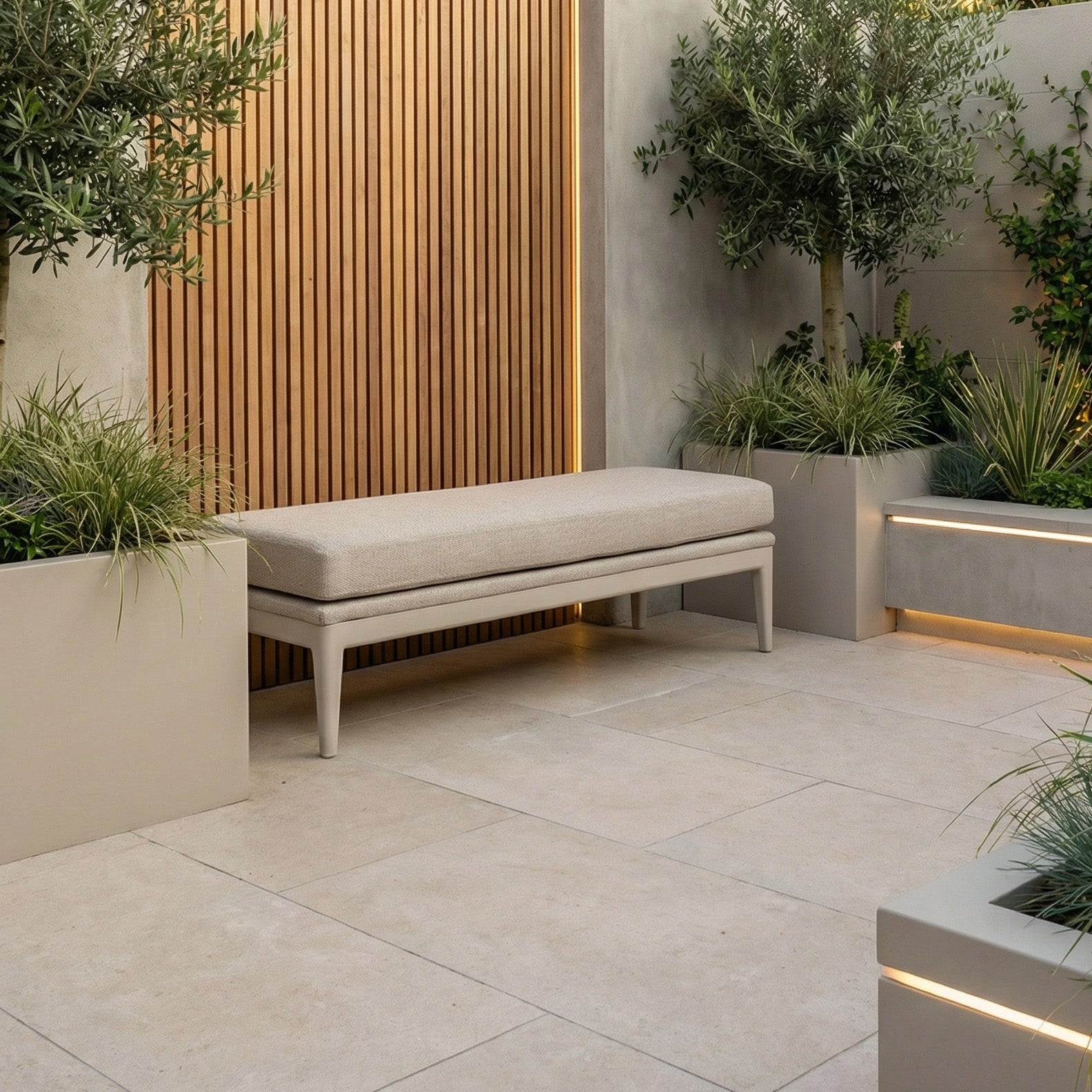 Modern patio with a Luna Bench in Fawn offering stylish outdoor seating, complemented by large planter boxes, lush green plants, and a vertical wooden slat wall.
