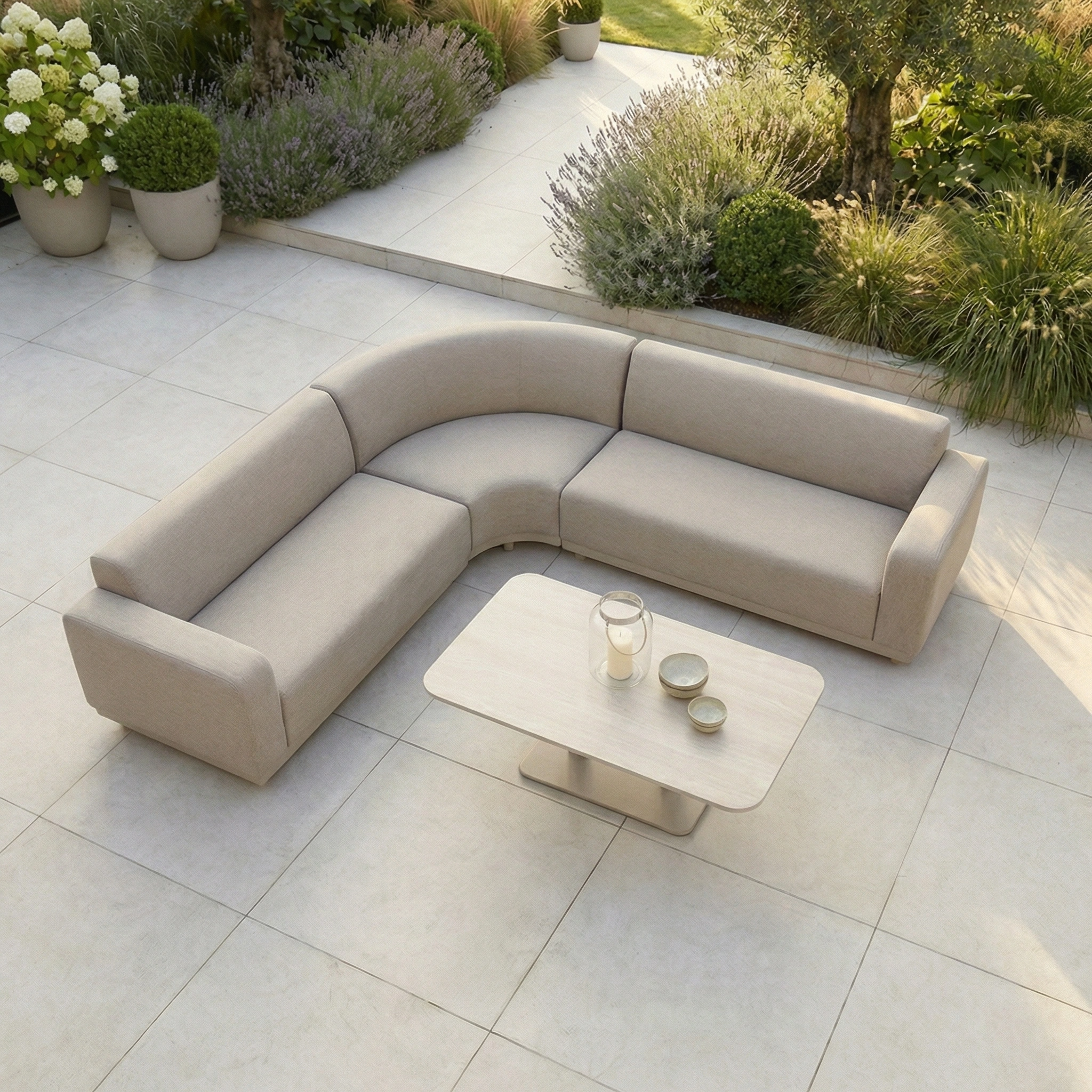 The Luna Outdoor Fabric Curved Corner Sofa Set with Altura Rising Table in Fawn is ideal all-weather garden furniture for relaxing outdoors, featuring a curved sofa and rising table on a tiled patio, surrounded by greenery.