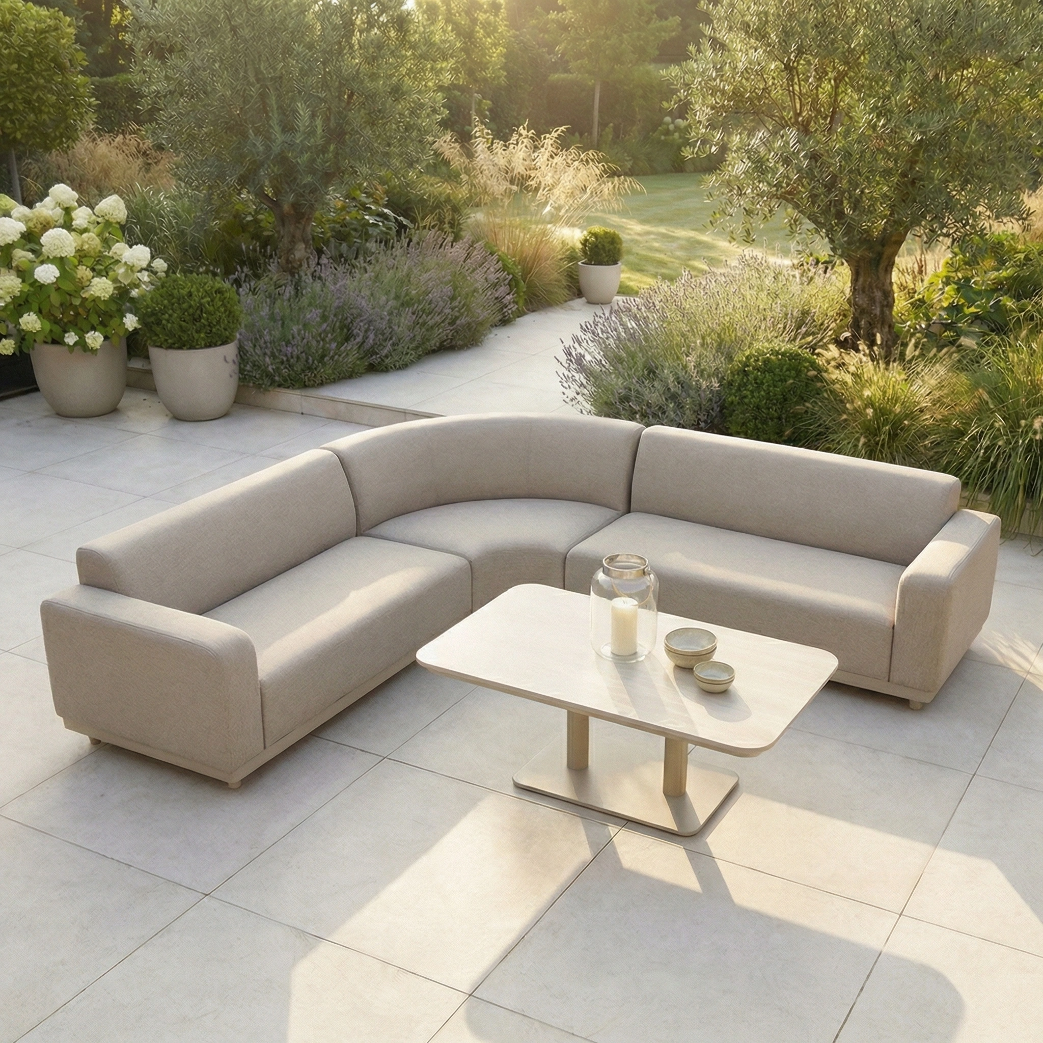 The Luna Outdoor Fabric Curved Corner Sofa Set with Altura Rising Table in Fawn sits on a tiled patio, surrounded by lush greenery and plants.