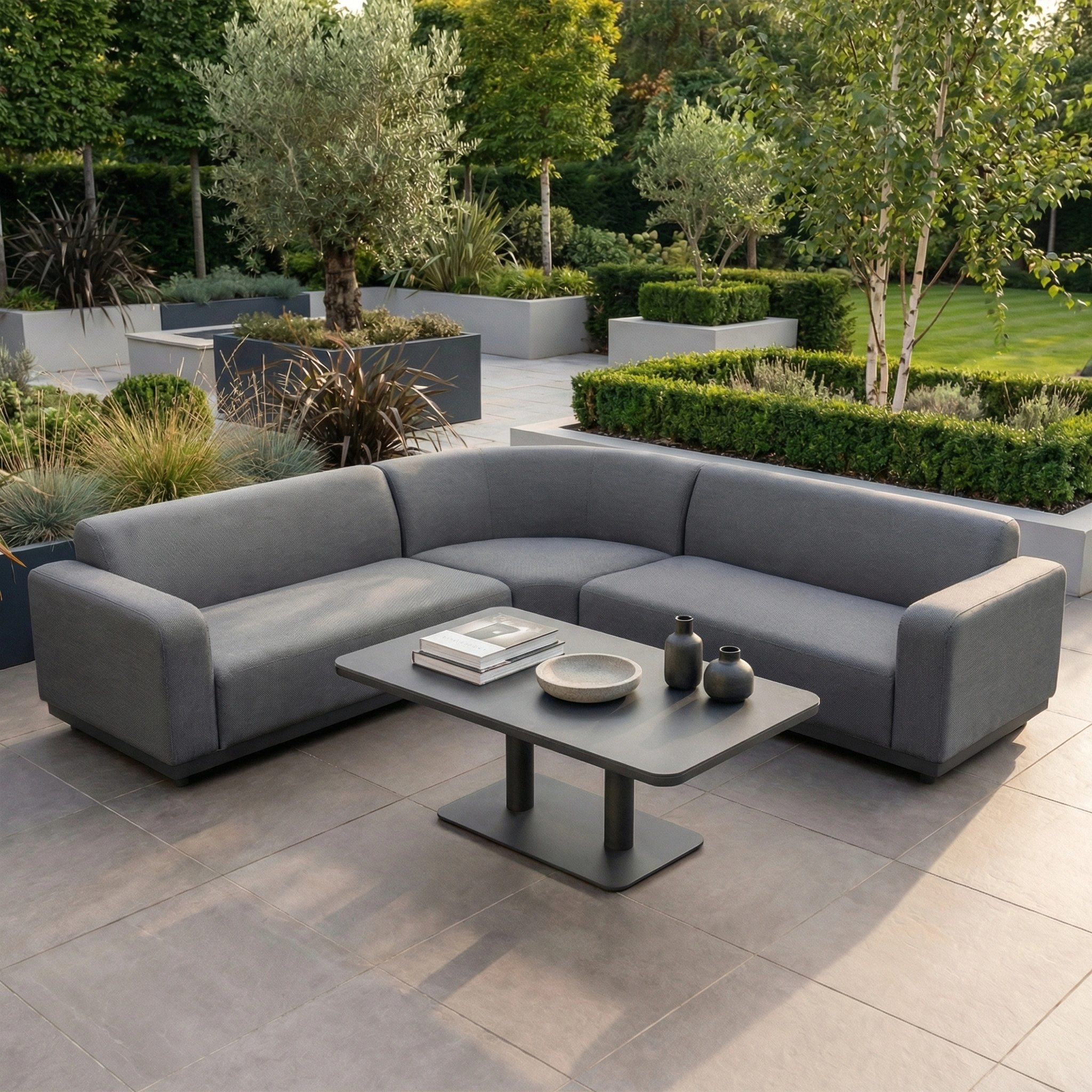 The Luna Outdoor Fabric Curved Corner Sofa Set with Altura Rising Table in Grey offers inviting, all-weather patio seating, perfect for relaxing among lush greenery on your tiled terrace.