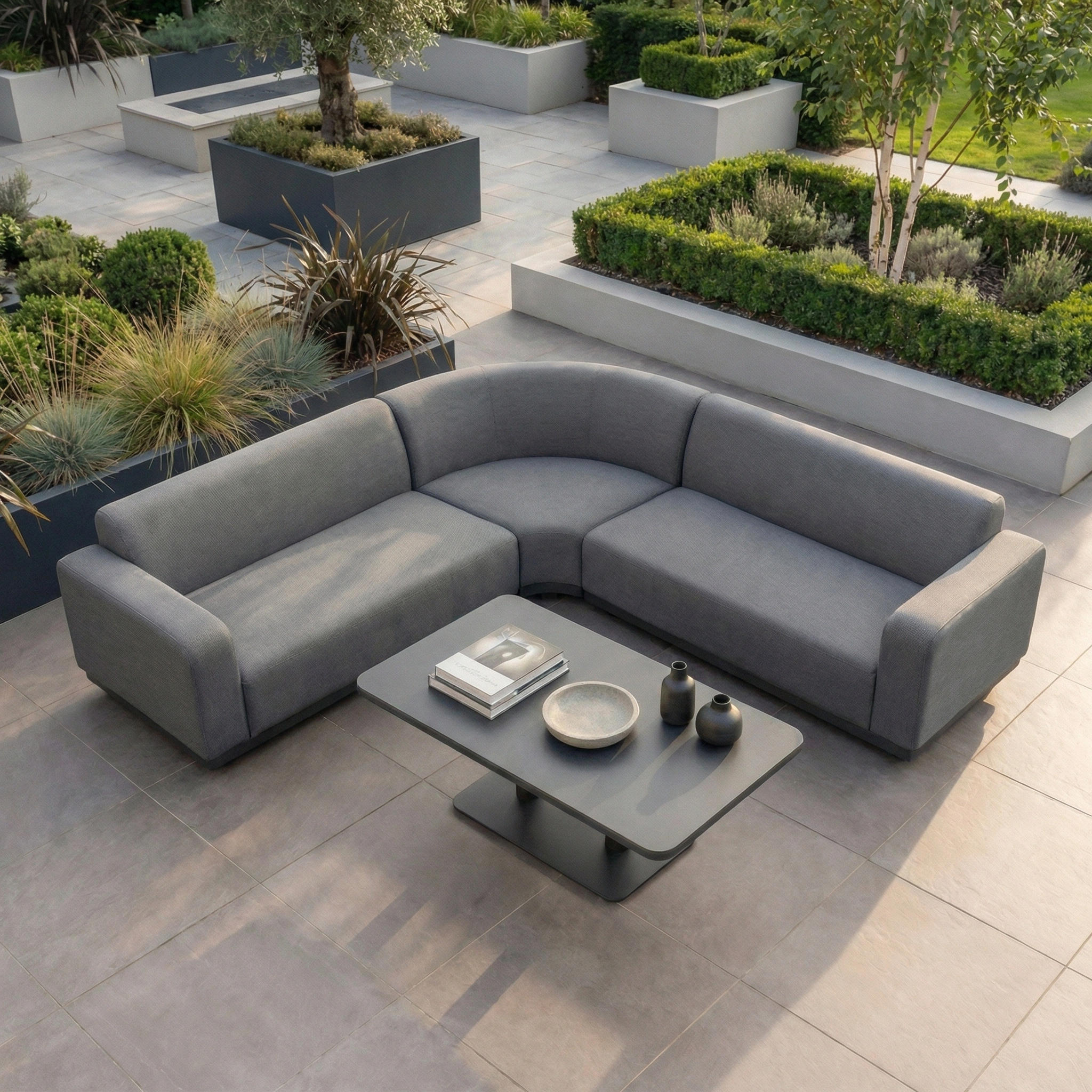 The Luna Outdoor Fabric Curved Corner Sofa Set with Altura Rising Table in Grey offers a stylish, modern look—perfect for your tiled patio and surrounded by greenery, it's an elegant addition to any all-weather garden furniture collection.