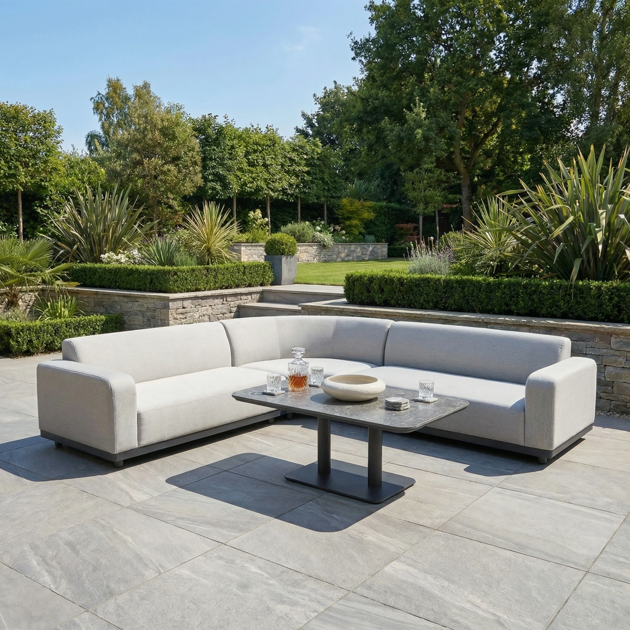 Create a stylish and inviting retreat with the Luna Outdoor Fabric Curved Corner Sofa Set and Altura Rising Table in Oyster Grey, perfect for relaxing in your garden patio surrounded by lush greenery.