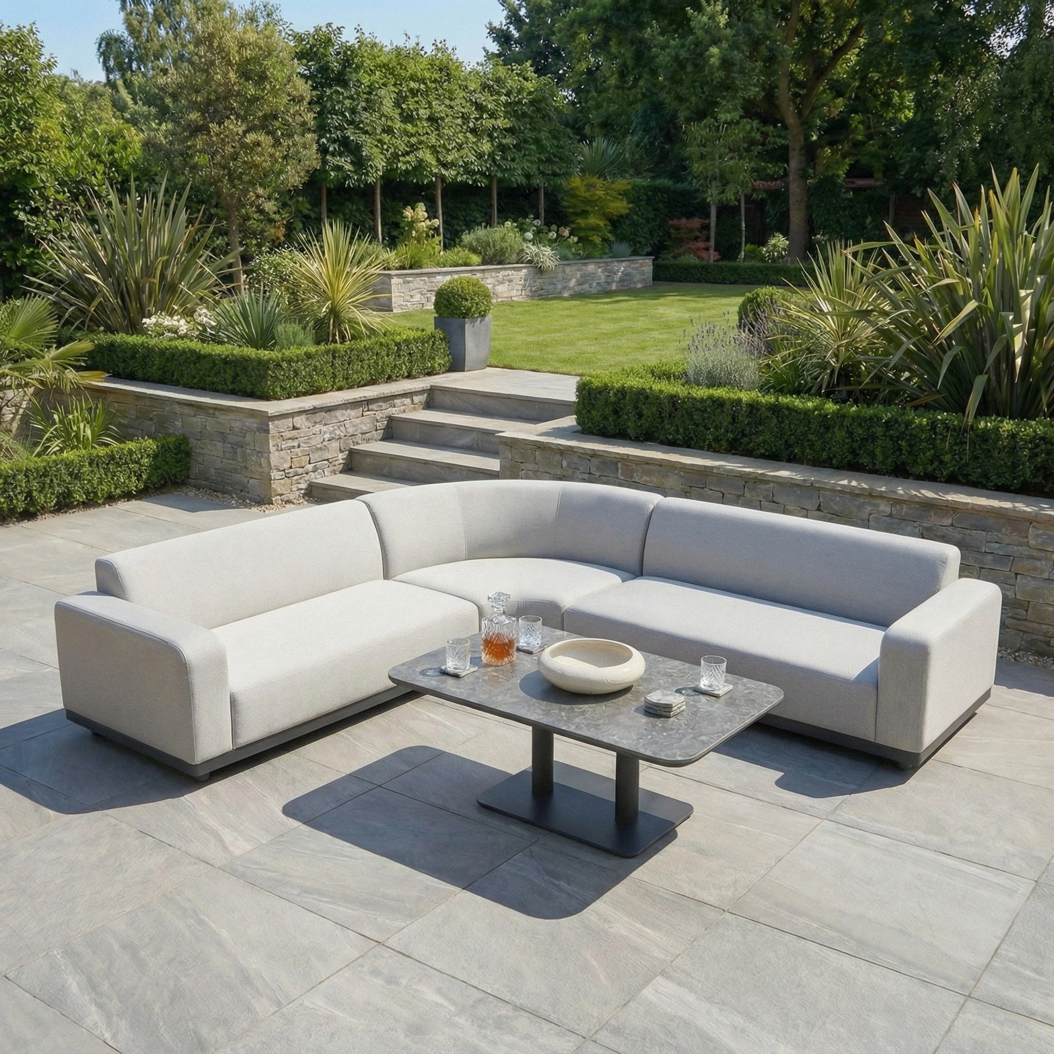 The Luna Outdoor Fabric Curved Corner Sofa Set with Altura Rising Table in Oyster Grey creates a stylish modern patio, ideal for relaxing afternoons amid lush greenery—durable all-weather garden furniture for outdoor comfort.
