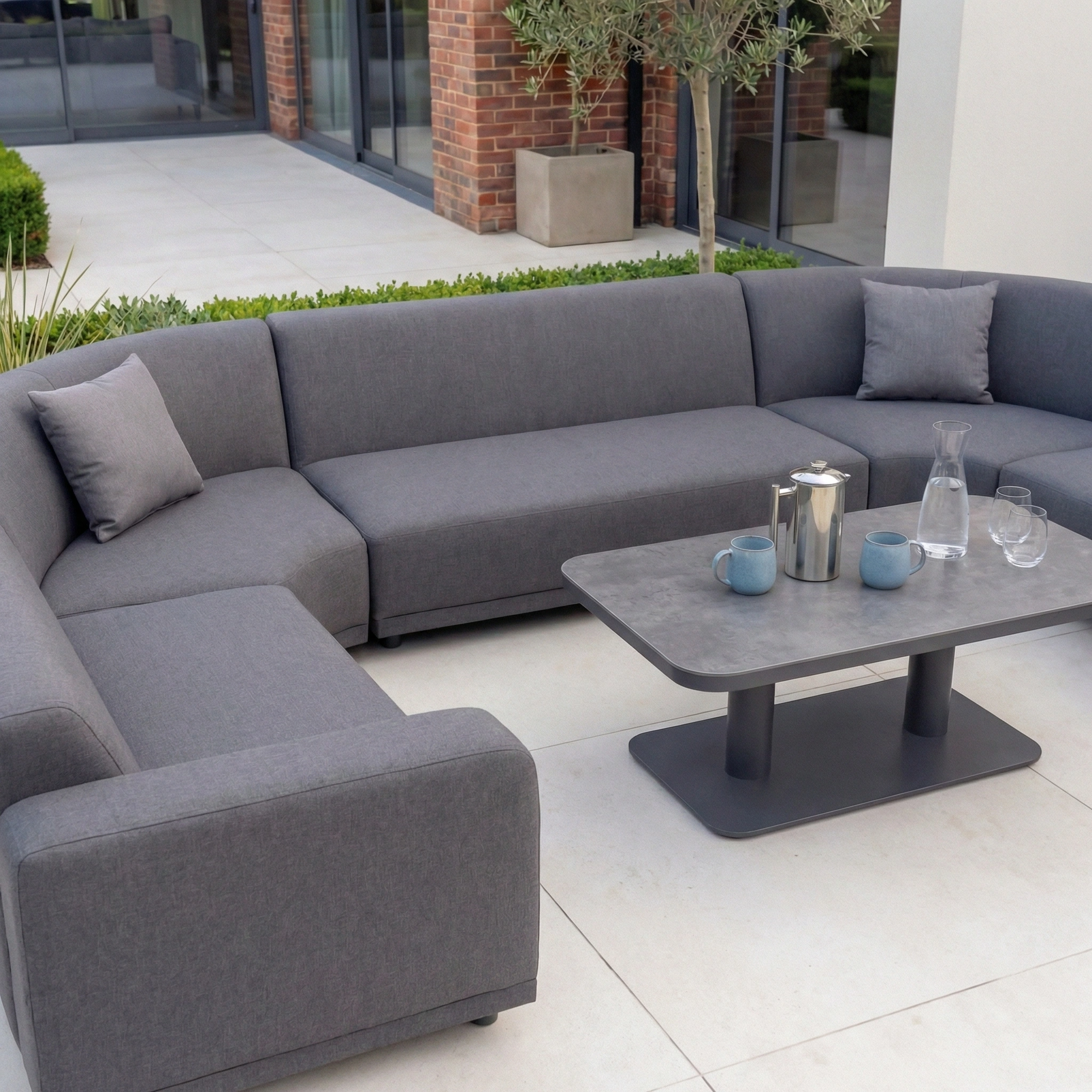 The Luna Outdoor Fabric Curved U-Shape Sofa Set in grey features all-weather material and comes with an Altura Rising Table, perfect for outdoor drinks and gatherings.