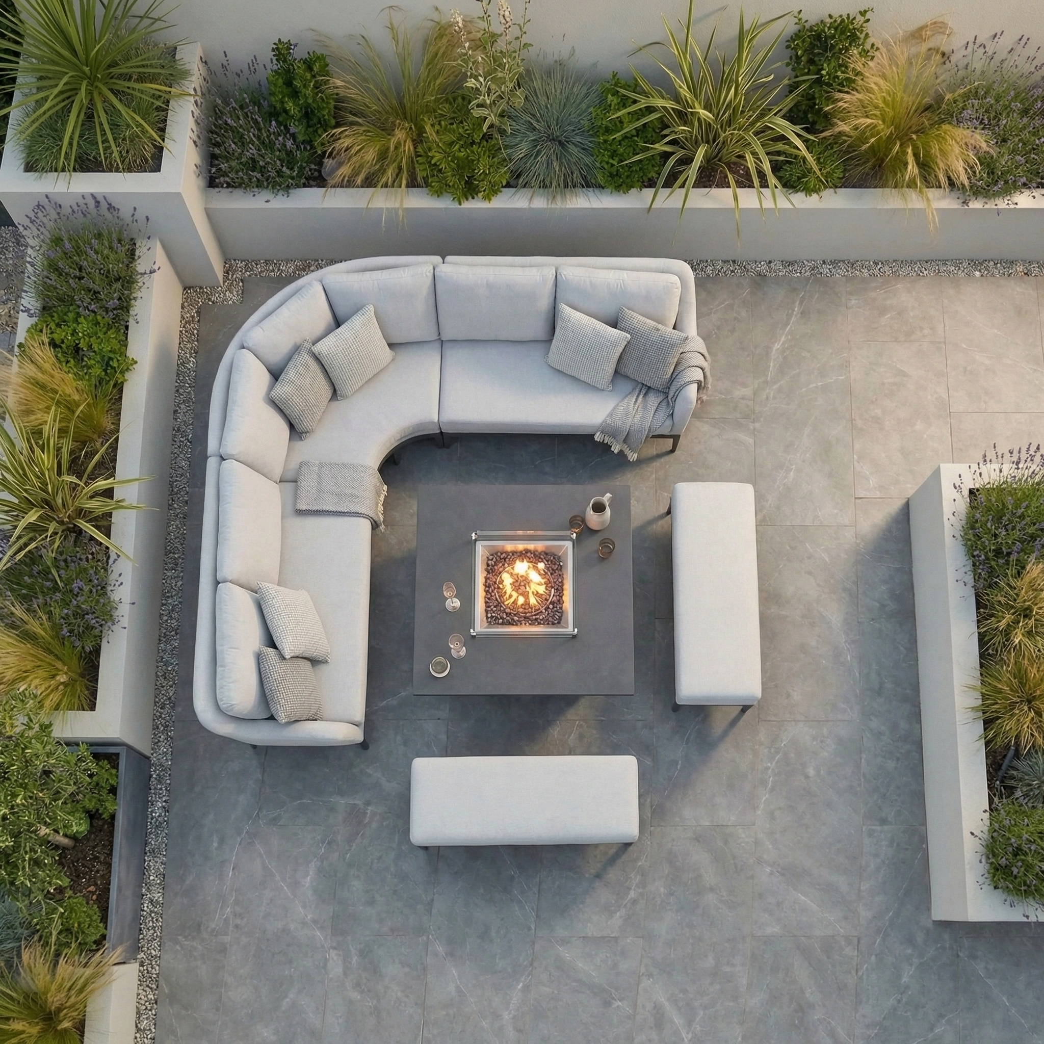 An overhead view of a modern patio featuring the Luna Deluxe Outdoor Fabric Square Corner Dining Set with Rising Firepit Table in Oyster Grey, complemented by benches and garden planters.