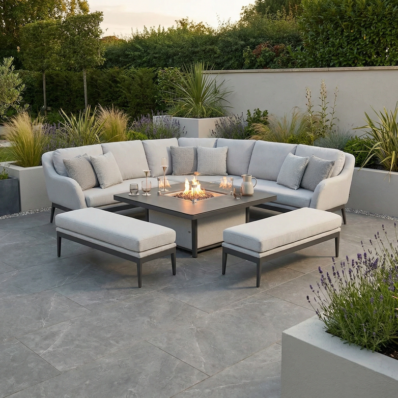 Modern patio with the Luna Deluxe Outdoor Fabric Square Corner Dining Set featuring a rising firepit table in Oyster Grey, set amidst lush greenery.