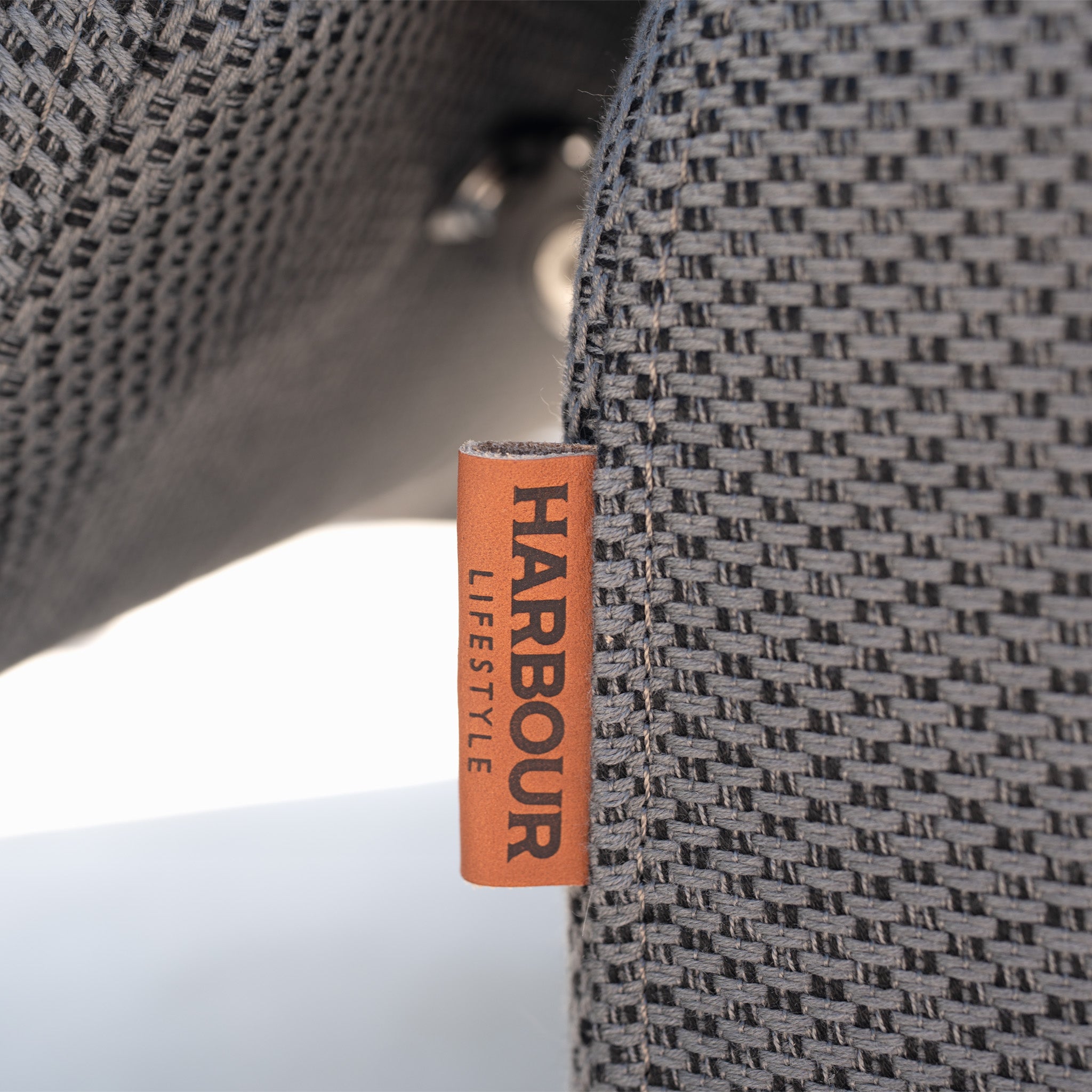 Close-up of woven grey Luna outdoor fabric with a brown HARBOUR LIFESTYLE tag, featured on the Luna Outdoor Fabric Deluxe Sun Lounger with Bolster Cushion in Grey.