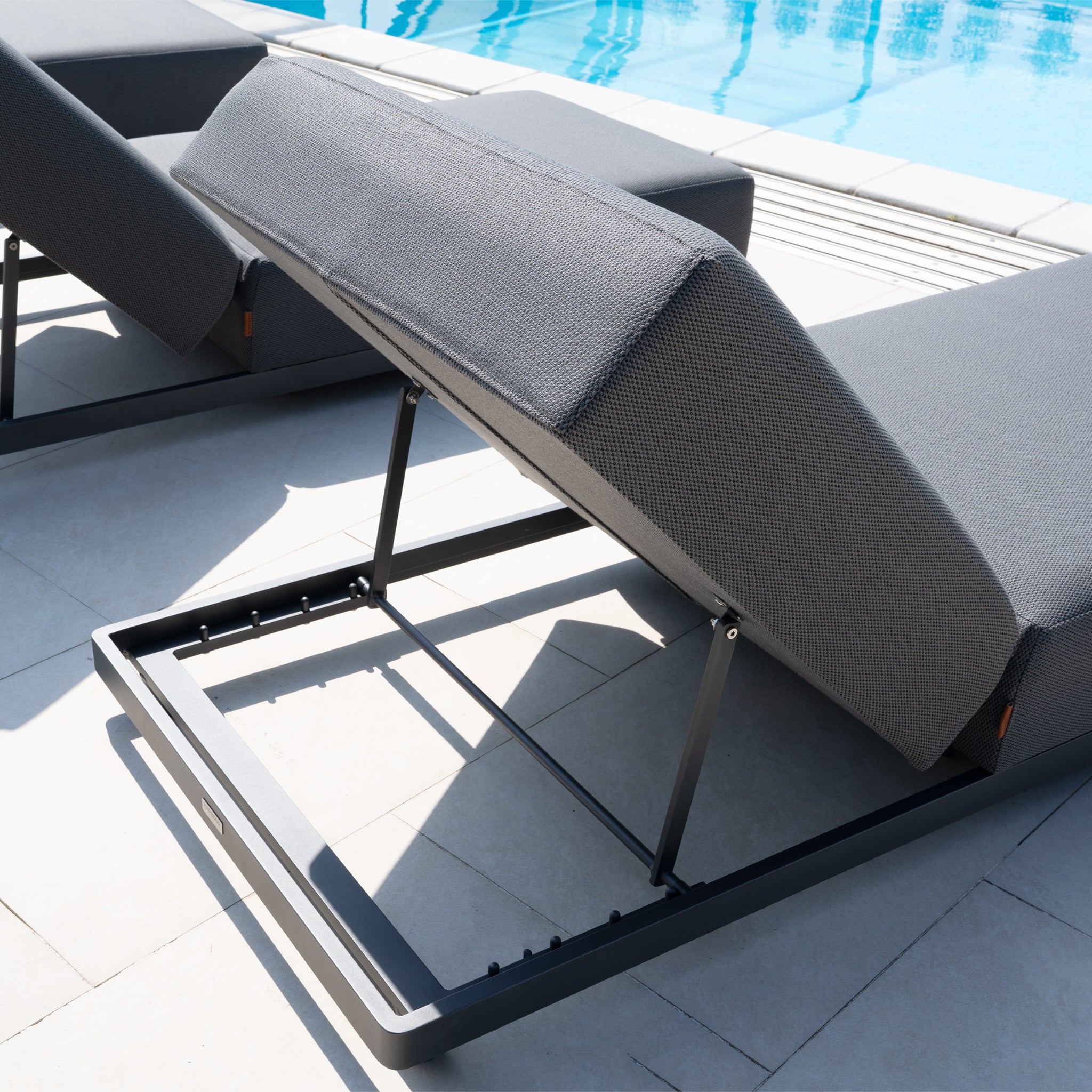 Close-up of the Luna Outdoor Fabric Deluxe Sun Lounger with Bolster Cushion in Grey, featuring an adjustable backrest and durable fabric, placed beside a sparkling blue swimming pool.