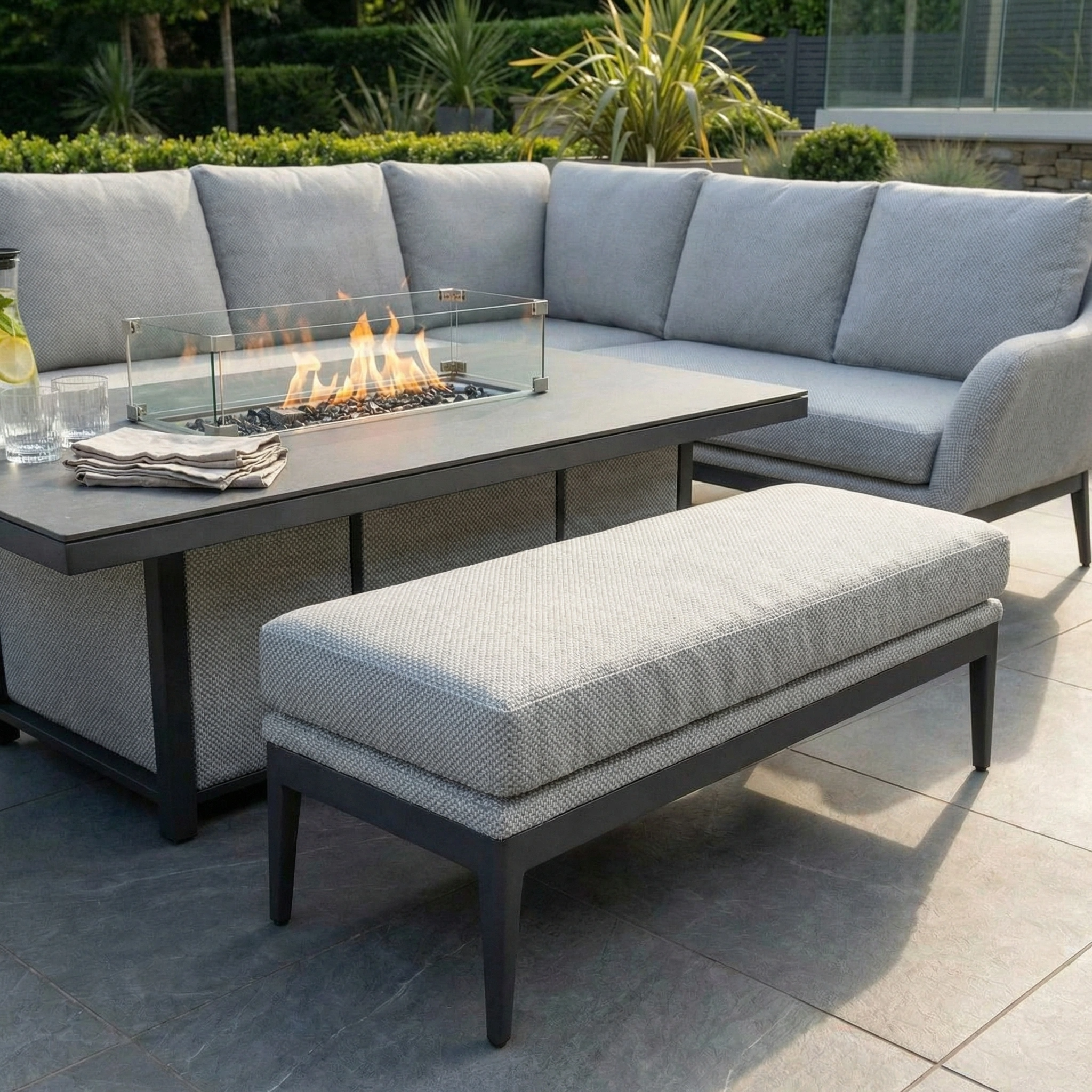 The Luna Outdoor Fabric Rectangular Corner Dining Set with Rising Firepit Table in Oyster Grey (Right Hand) features plush cushions and a sleek bench, perfect for outdoor dining on a tiled terrace.