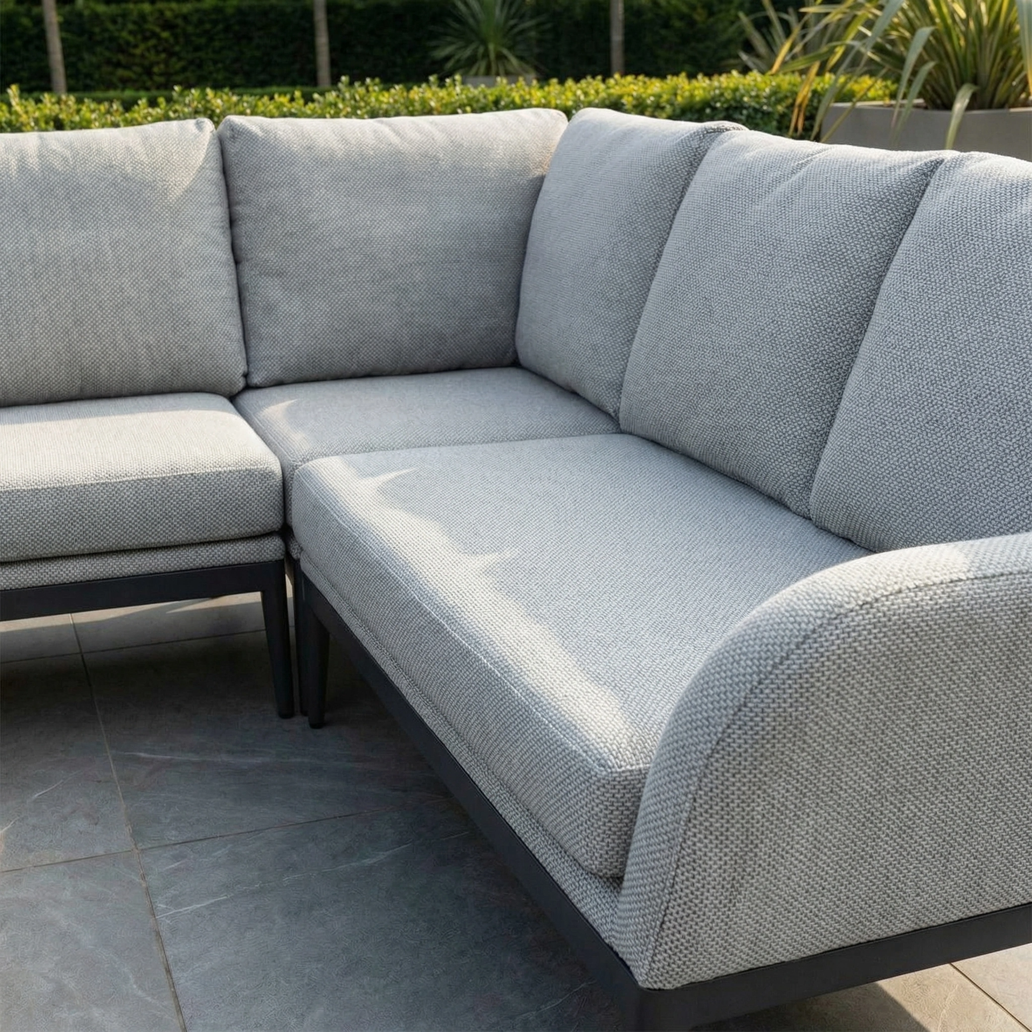 Luna Outdoor Fabric Rectangular Corner Dining Set with Rising Firepit Table in Oyster Grey (Right Hand) on a stone patio, featuring plush cushions and lush green landscaping in the background.
