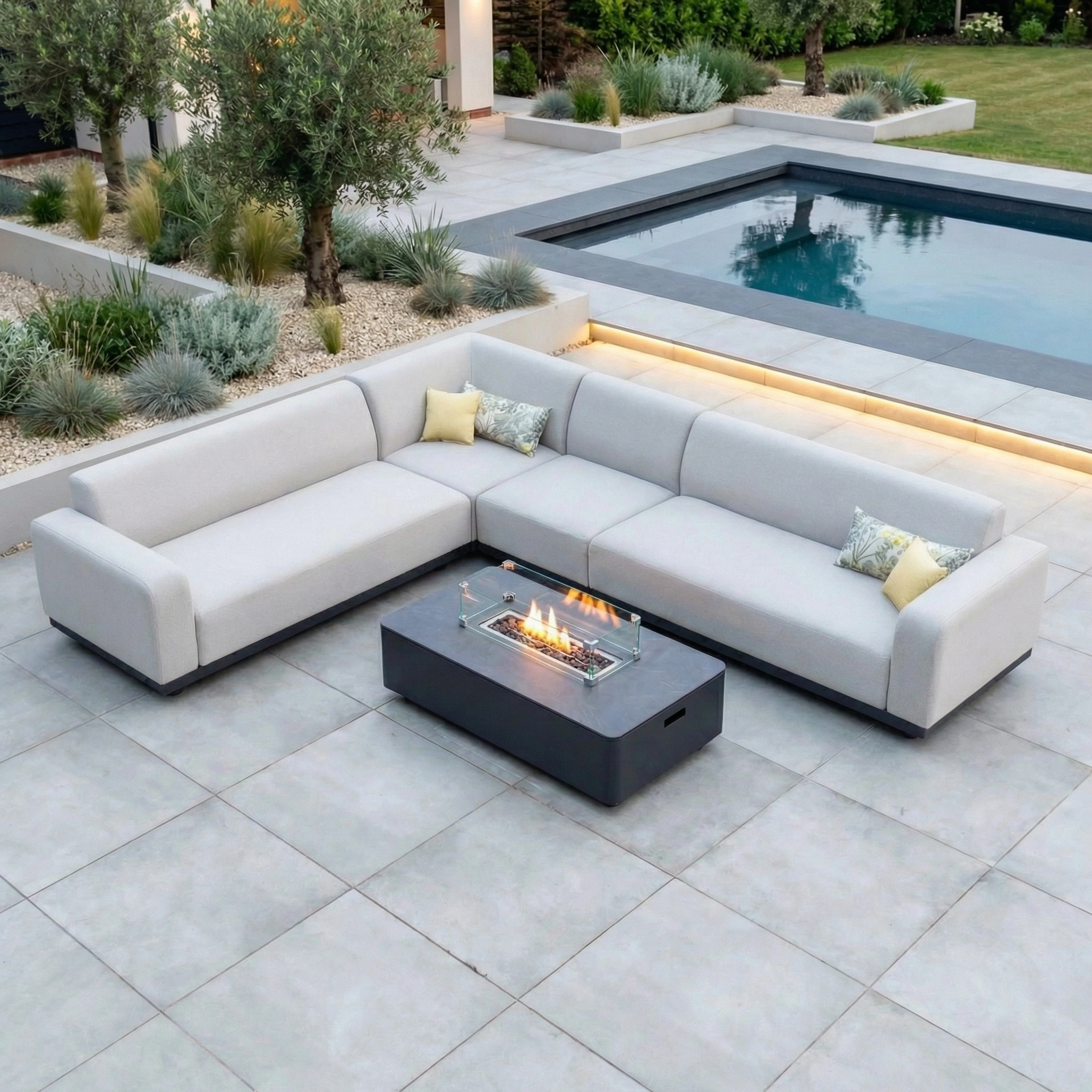 Modern patio featuring the Luna Outdoor Fabric Large Corner Group Set with Firepit Coffee Table in Oyster Grey, complemented by a pool and lush greenery.