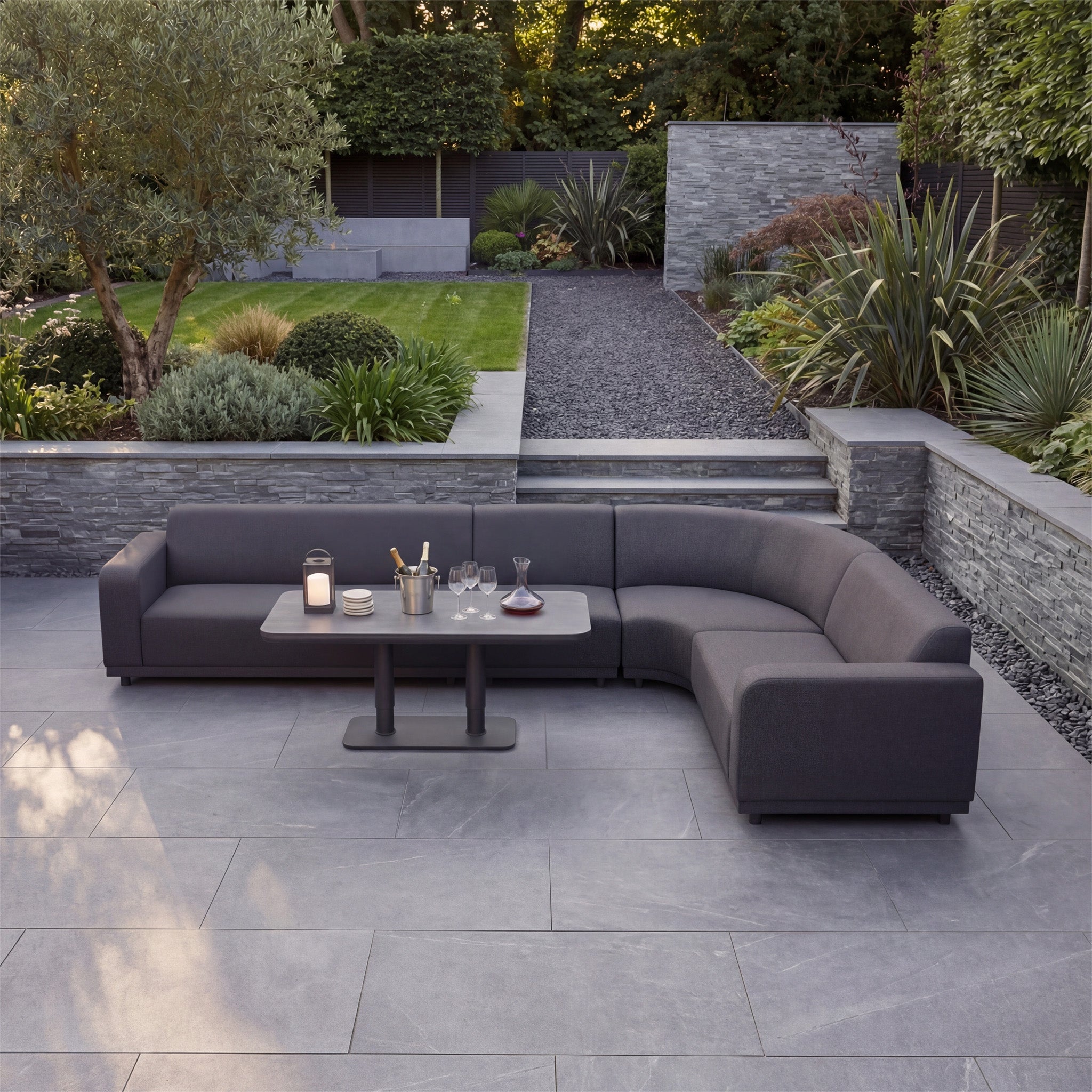 Modern outdoor seating area with a Luna Outdoor Fabric Large Curved Corner Sofa Set and Altura Rising Table in Grey, complemented by drinks on the table.