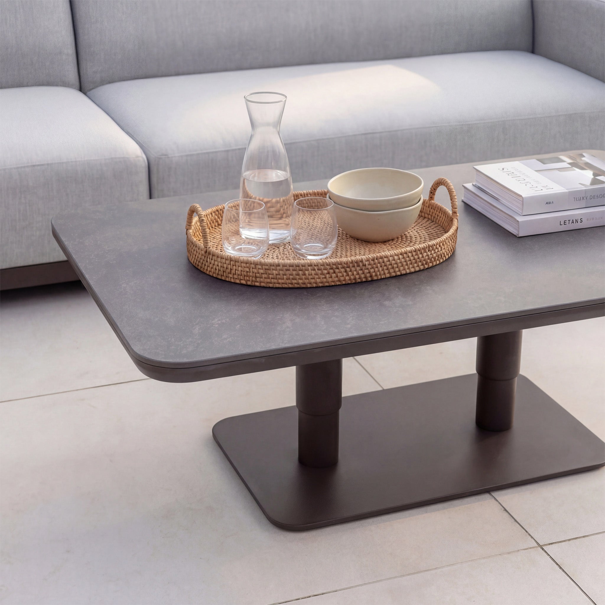 The Luna Outdoor Fabric Large Curved Corner Sofa Set with Altura Rising Table in Oyster Grey features a modern tray with a carafe, glass, bowl, and books—ideal for all-weather durability and contemporary style.