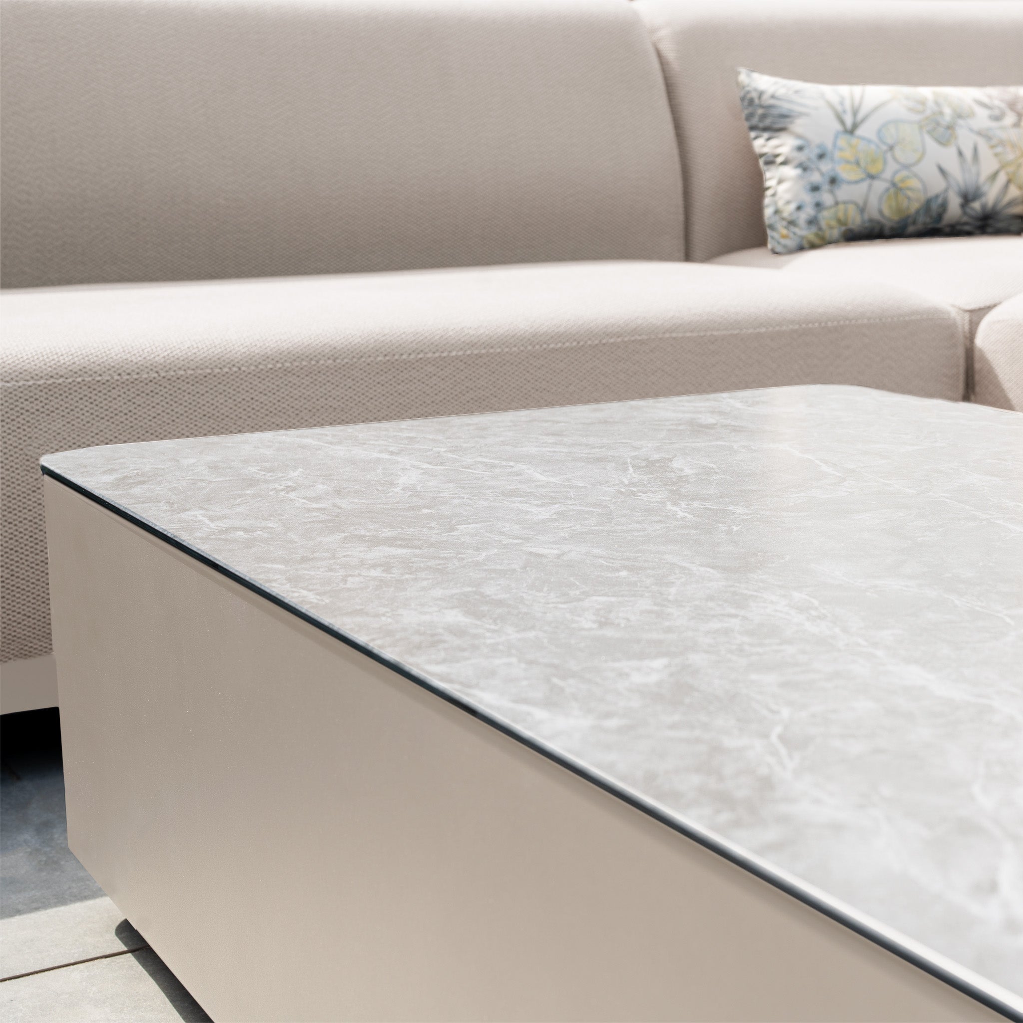 Close-up of a marble coffee table and a light beige Luna Outdoor Fabric Large Corner Group Set with floral pillow in durable fawn fabric by Harbour Lifestyle.