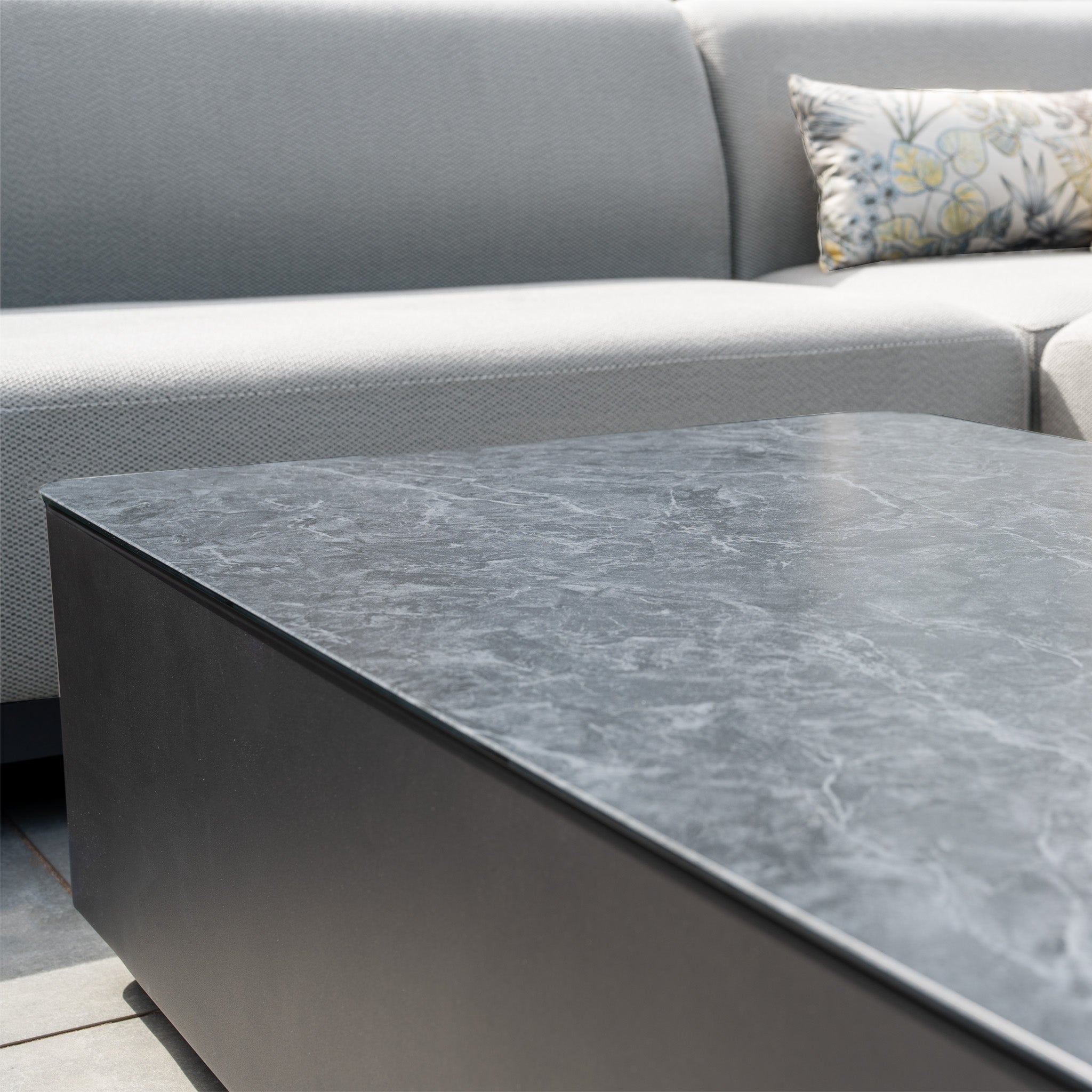 The Luna Outdoor Fabric Large Corner Group Set in Oyster Grey features a spacious sofa accented with a floral cushion and is paired with a black marble coffee table.