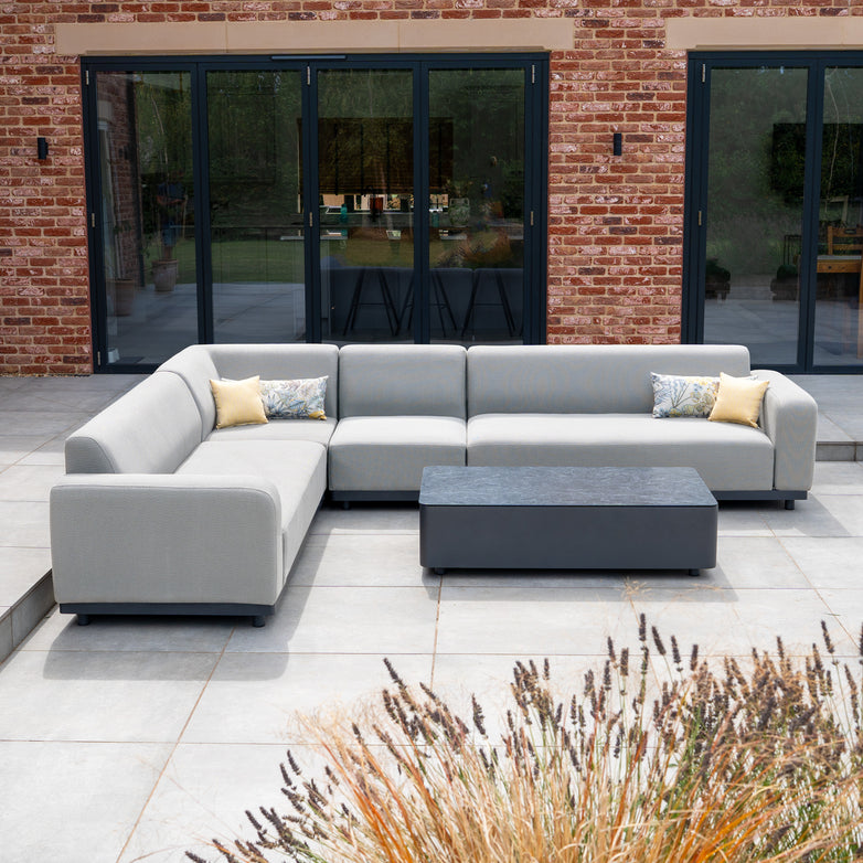 The Luna Outdoor Fabric Large Corner Group Set with Coffee Table in Oyster Grey offers elegant, stain-proof, all-weather garden seating—perfect for patios with its cushions and stylish coffee table in front of glass doors.