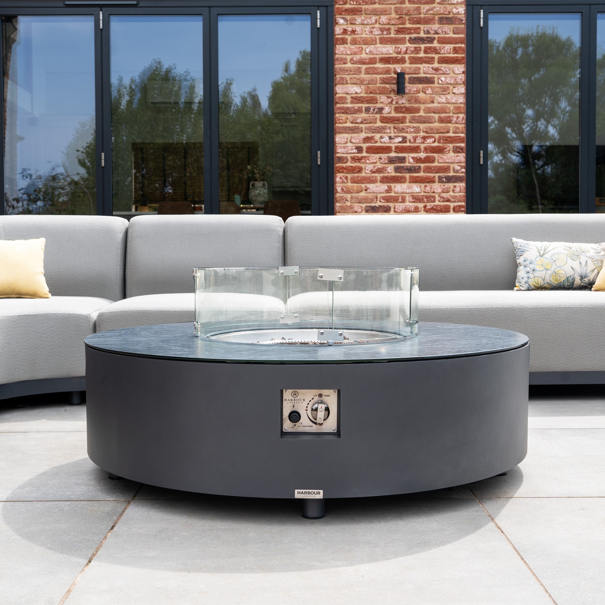 The Luna Outdoor Fabric Large Curved Corner Group Set with Round Firepit Coffee Table in Oyster Grey creates a stylish patio retreat, featuring a modern firepit and durable gray seating ideal for outdoor gatherings.