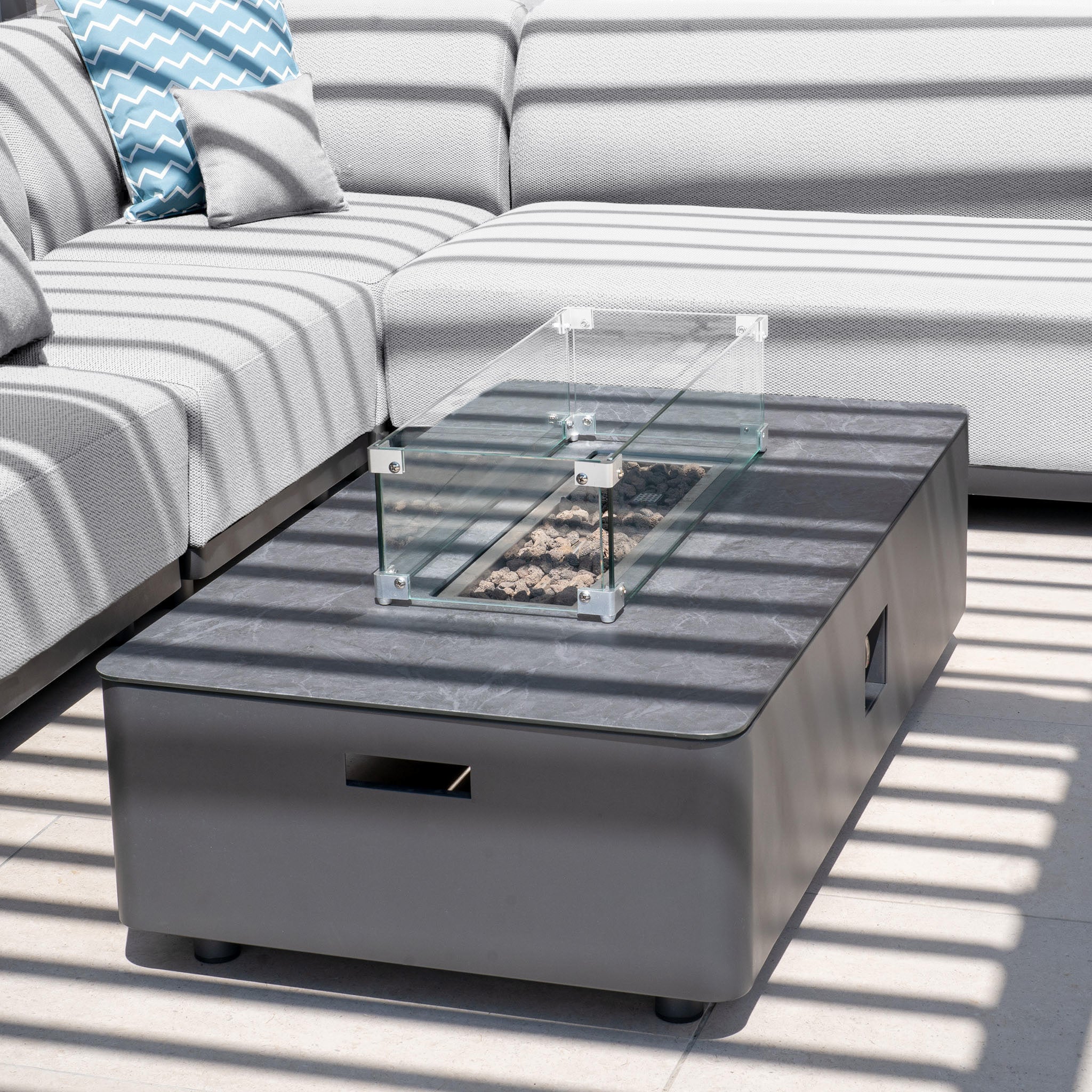 The modern outdoor seating set includes the Luna Outdoor Fabric Large Corner Group in Oyster Grey, paired with a firepit coffee table that casts striped shadows.