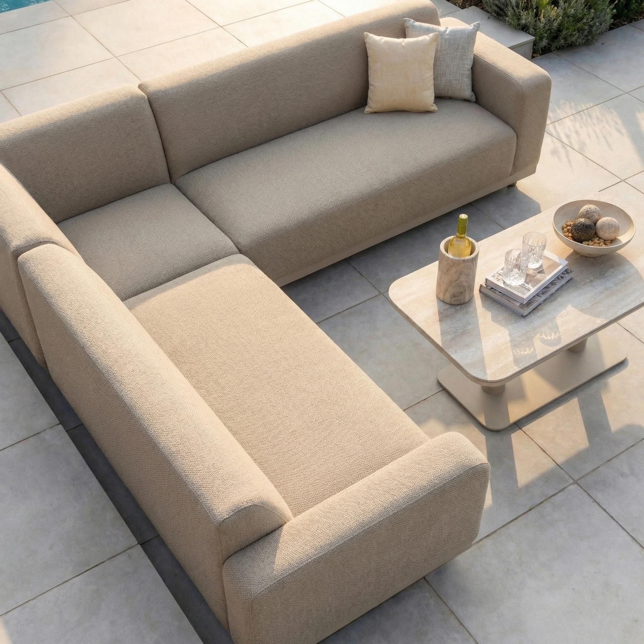 The Luna Outdoor Fabric Corner Sofa Set with Altura Rising Table in Fawn, crafted from stain-resistant, all-weather material, is arranged on a tiled patio beside the table set with drinks and snacks.