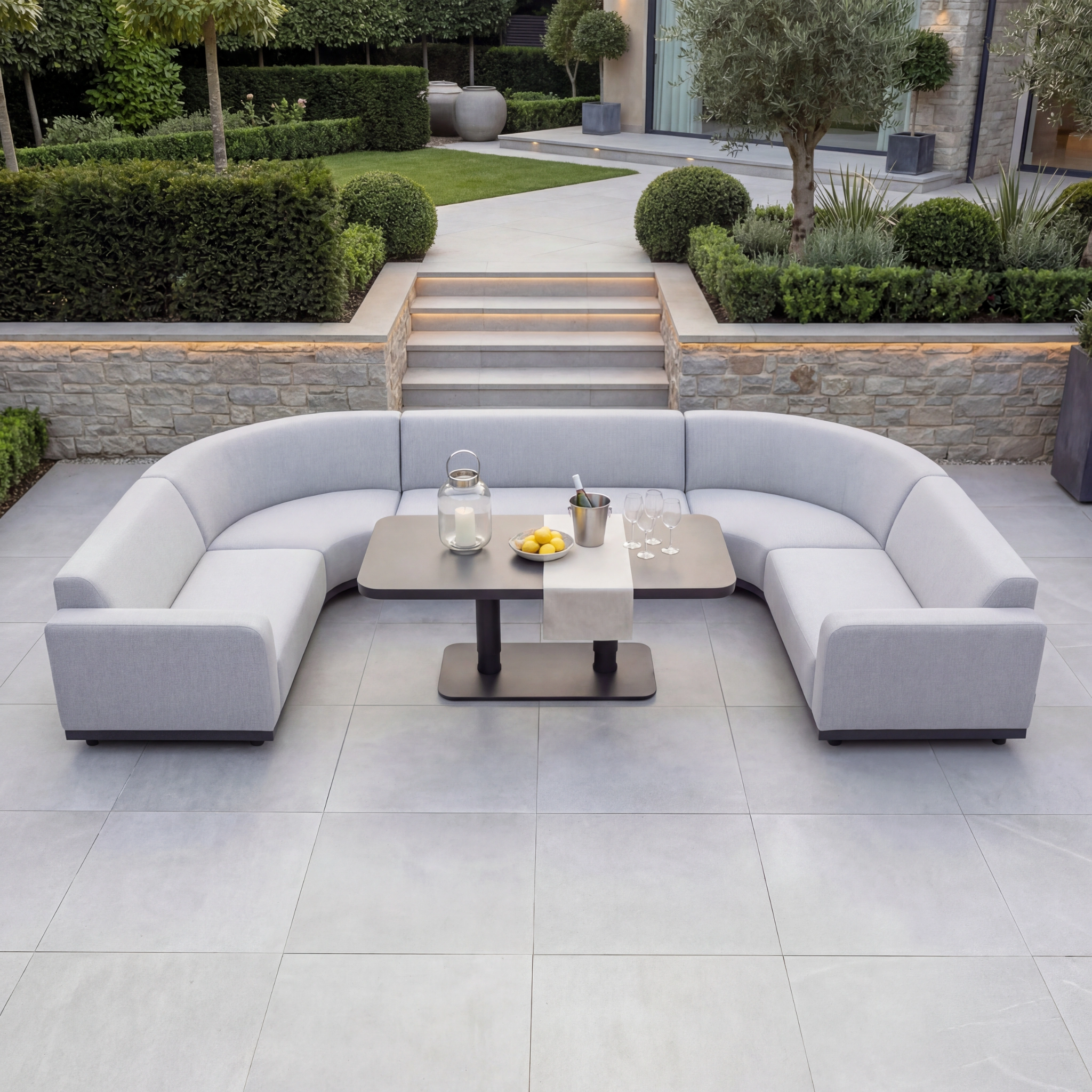The Luna Outdoor Fabric Curved U-Shape Sofa Set with Altura Rising Table in Oyster Grey is crafted from all-weather materials with solution-dyed acrylic, offering lasting style and comfort for your garden or patio.