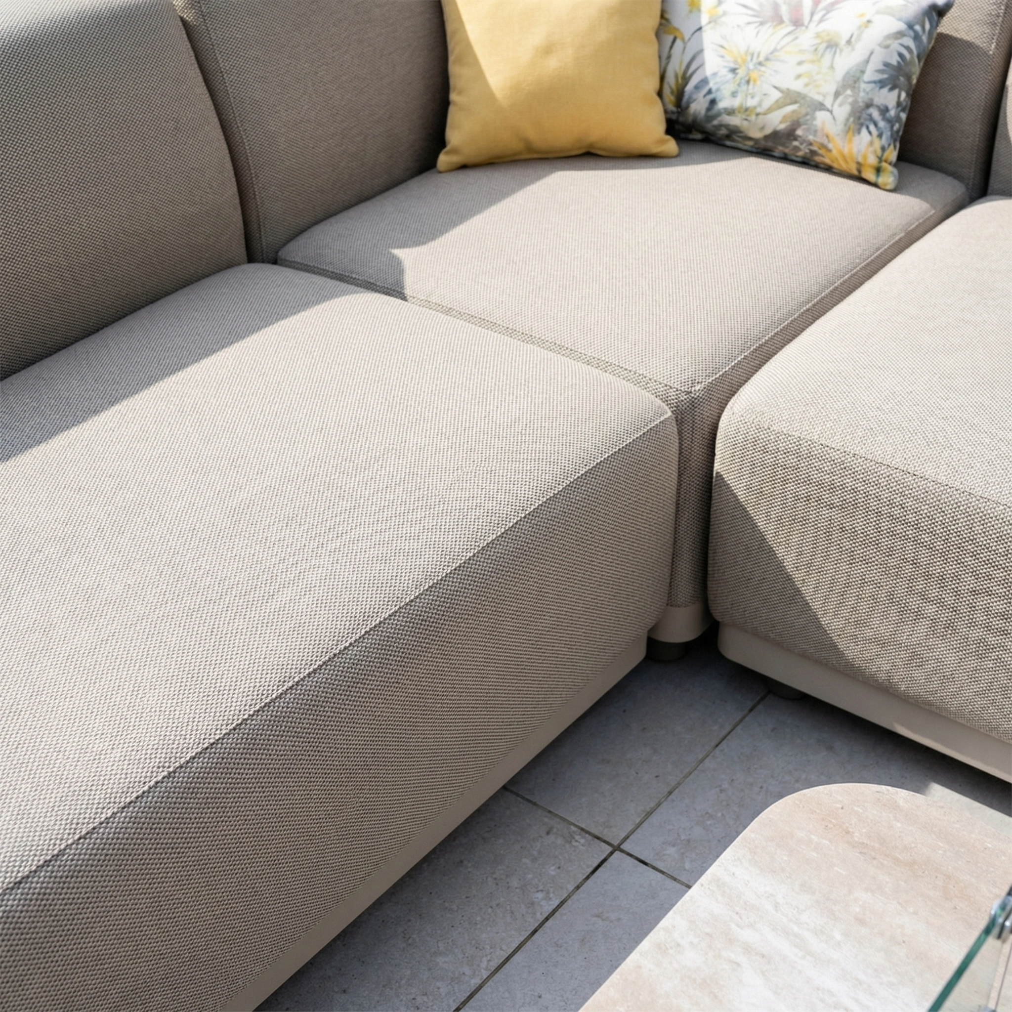 The Luna Outdoor Fabric Large Corner Group Set with Firepit Coffee Table in Fawn is a light gray sectional made from all-weather material, complemented by yellow and floral pillows.