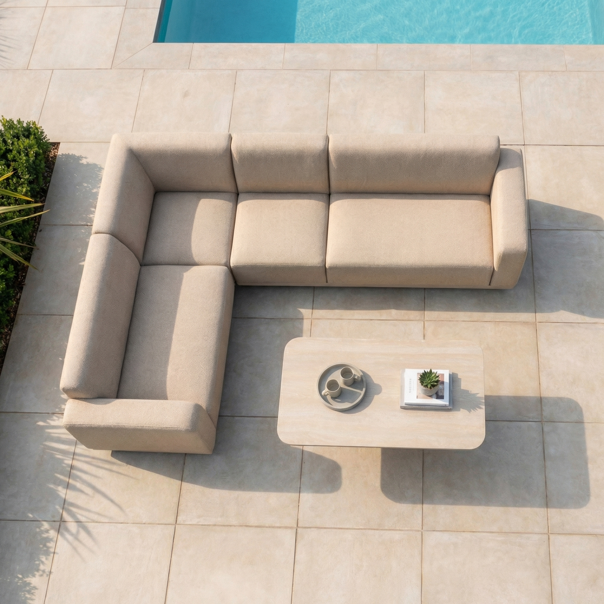 The Luna Outdoor Fabric Large Corner Sofa Set with Altura Rising Table in Fawn sits on a tiled patio beside a pool, viewed from above.