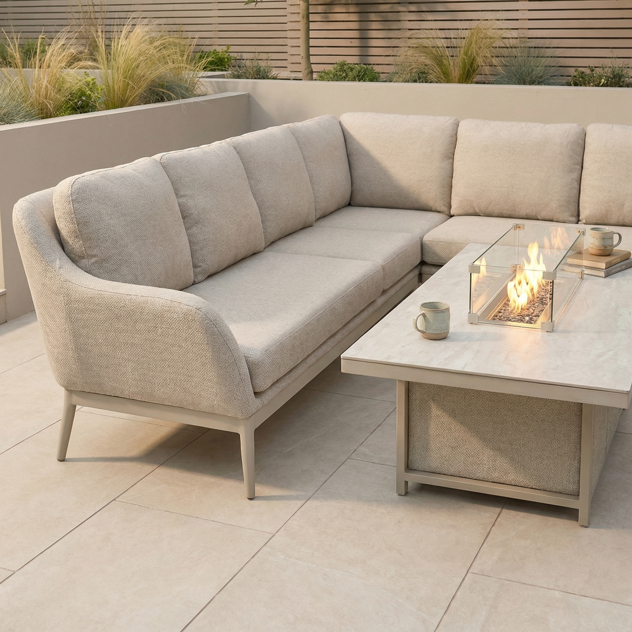 The Luna Outdoor Fabric Rectangular Corner Dining Set with Rising Firepit Table in Fawn (Right Hand) is shown on a tiled patio, featuring two mugs placed on the table.