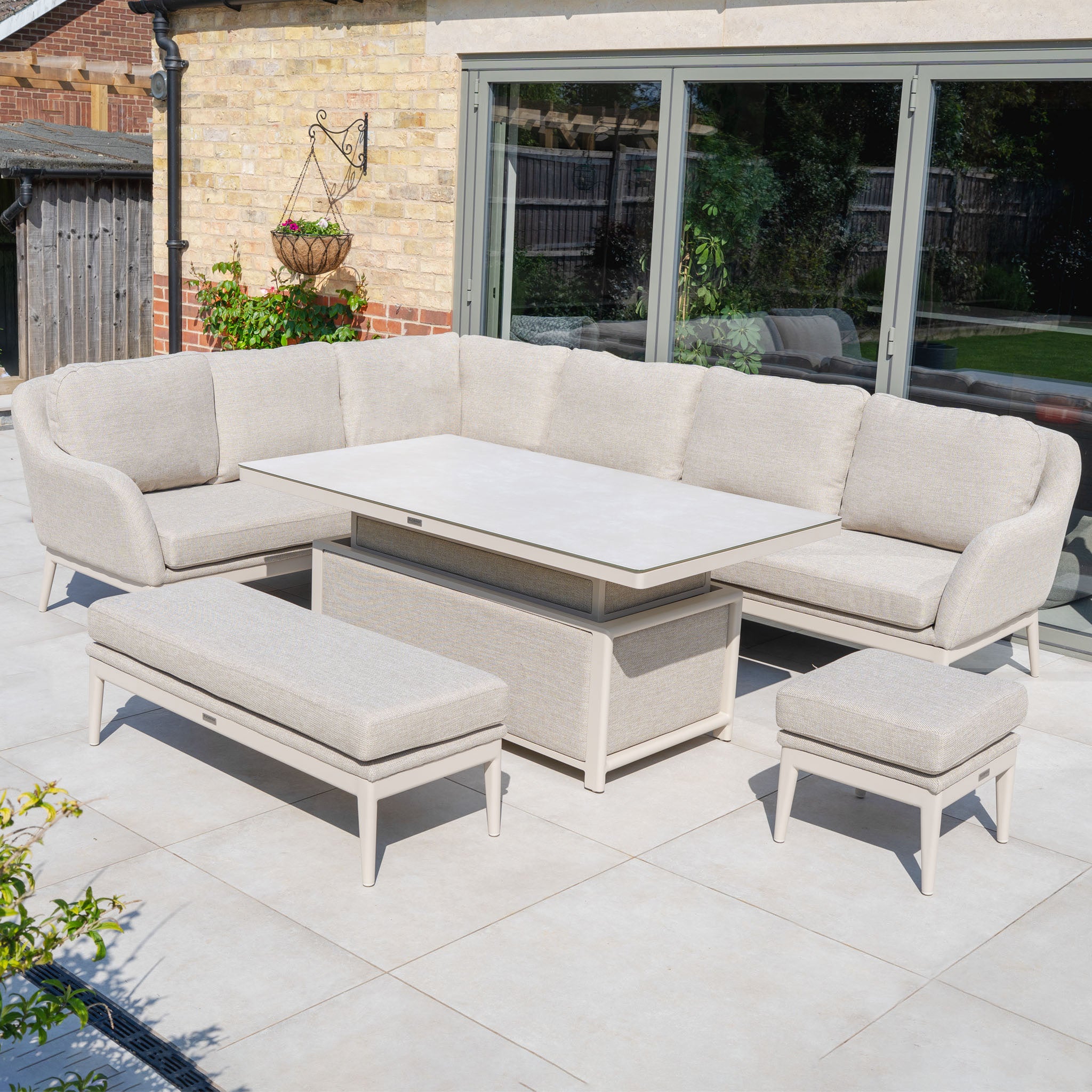 Luna Outdoor Fabric Rectangular Corner Dining Set with Rising Table in Fawn (Left Hand), arranged on a tiled patio beside a glass door, featuring a bench and stool.