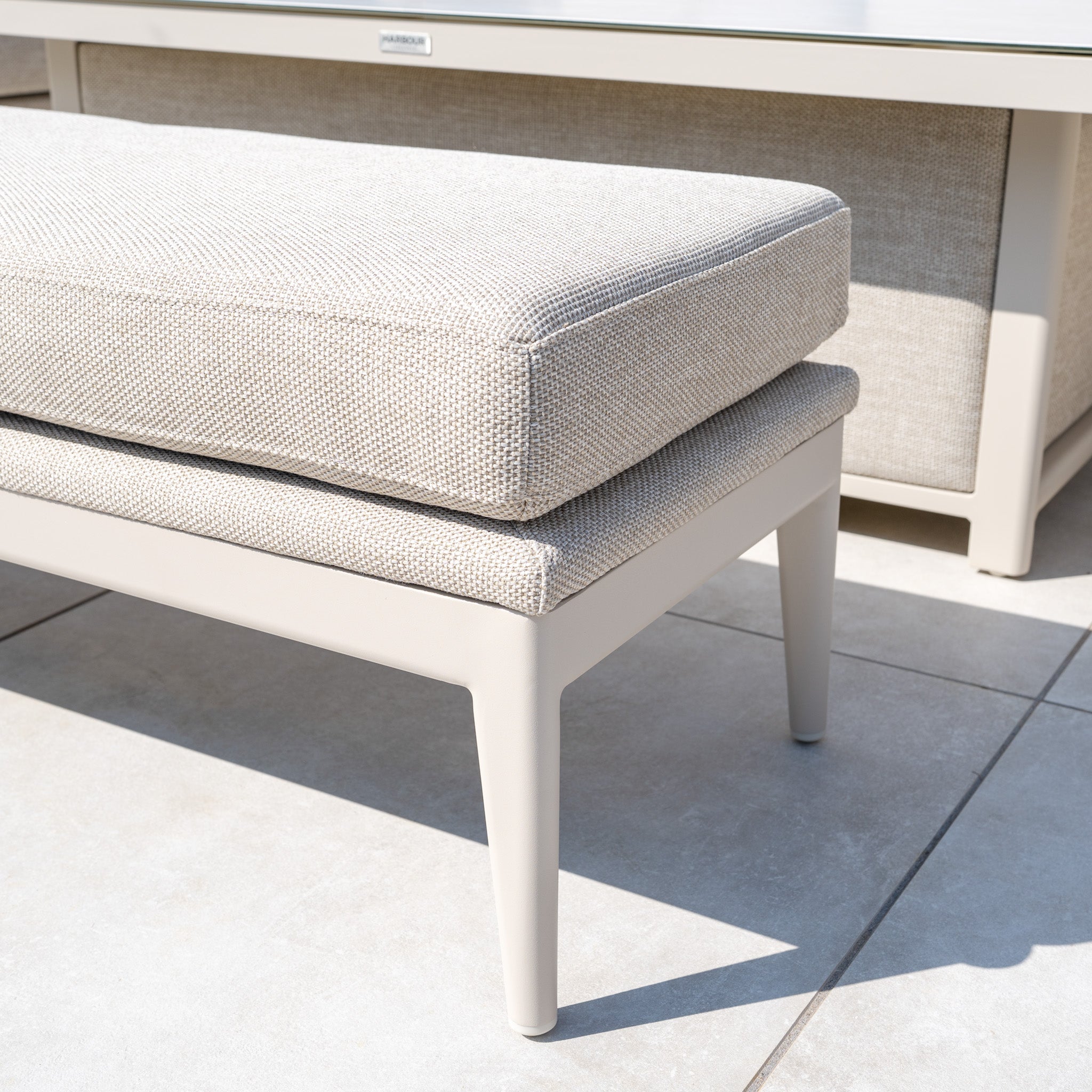 Luna Outdoor Fabric Rectangular Corner Dining Set with Rising Table in Fawn (Left Hand) features stain-proof cushioned seating, shown here on a tiled patio with sunlight casting shadows across the ground.