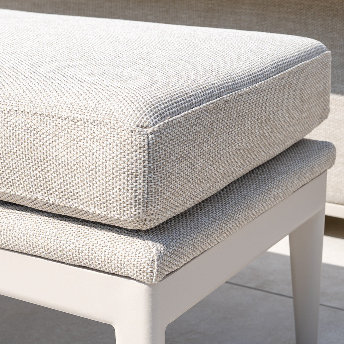 Close-up of two stacked light beige textured cushions on a white outdoor chair in sunlight, perfect for cozying up your Luna Bench in Fawn and enhancing your outdoor seating experience.