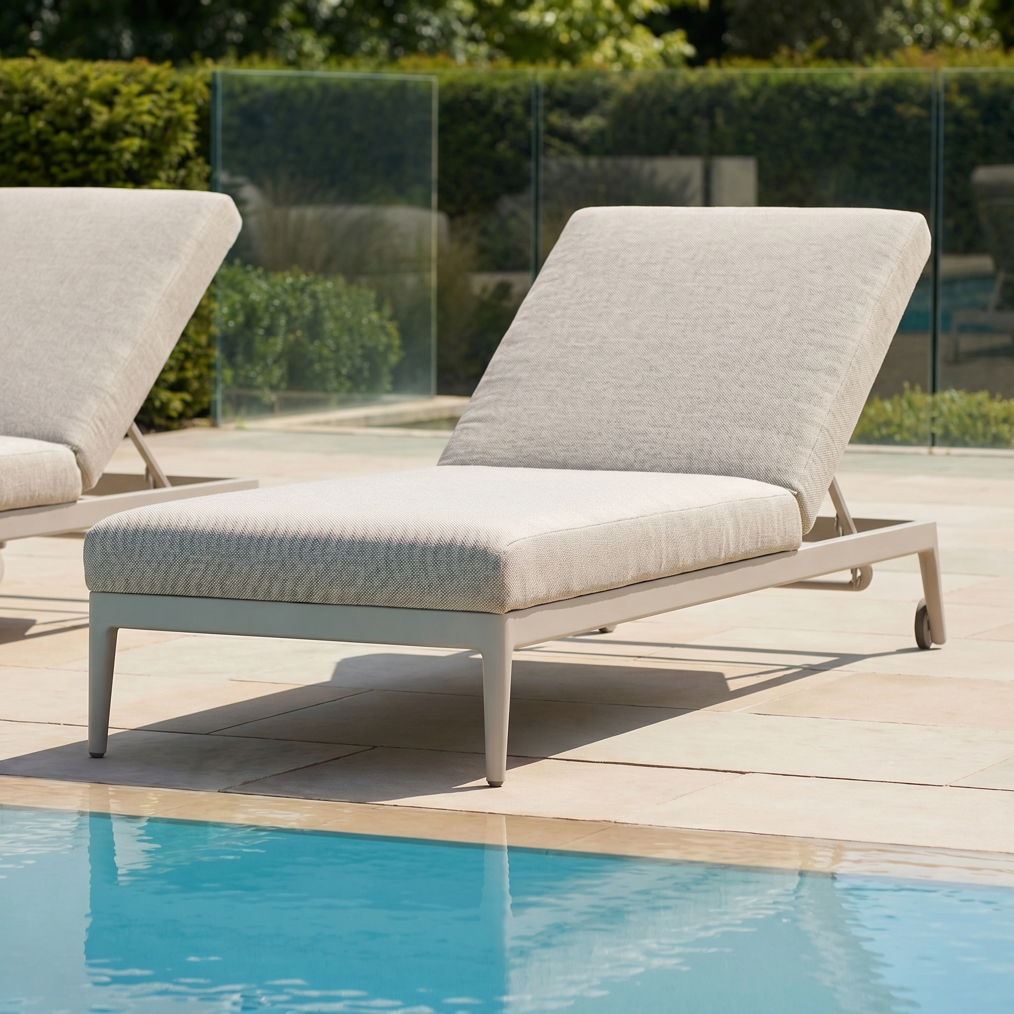 The Luna Outdoor Fabric Sun Lounger in Fawn sits by a sparkling pool on a sunny day, offering all-weather comfort with its durable cushioned design.